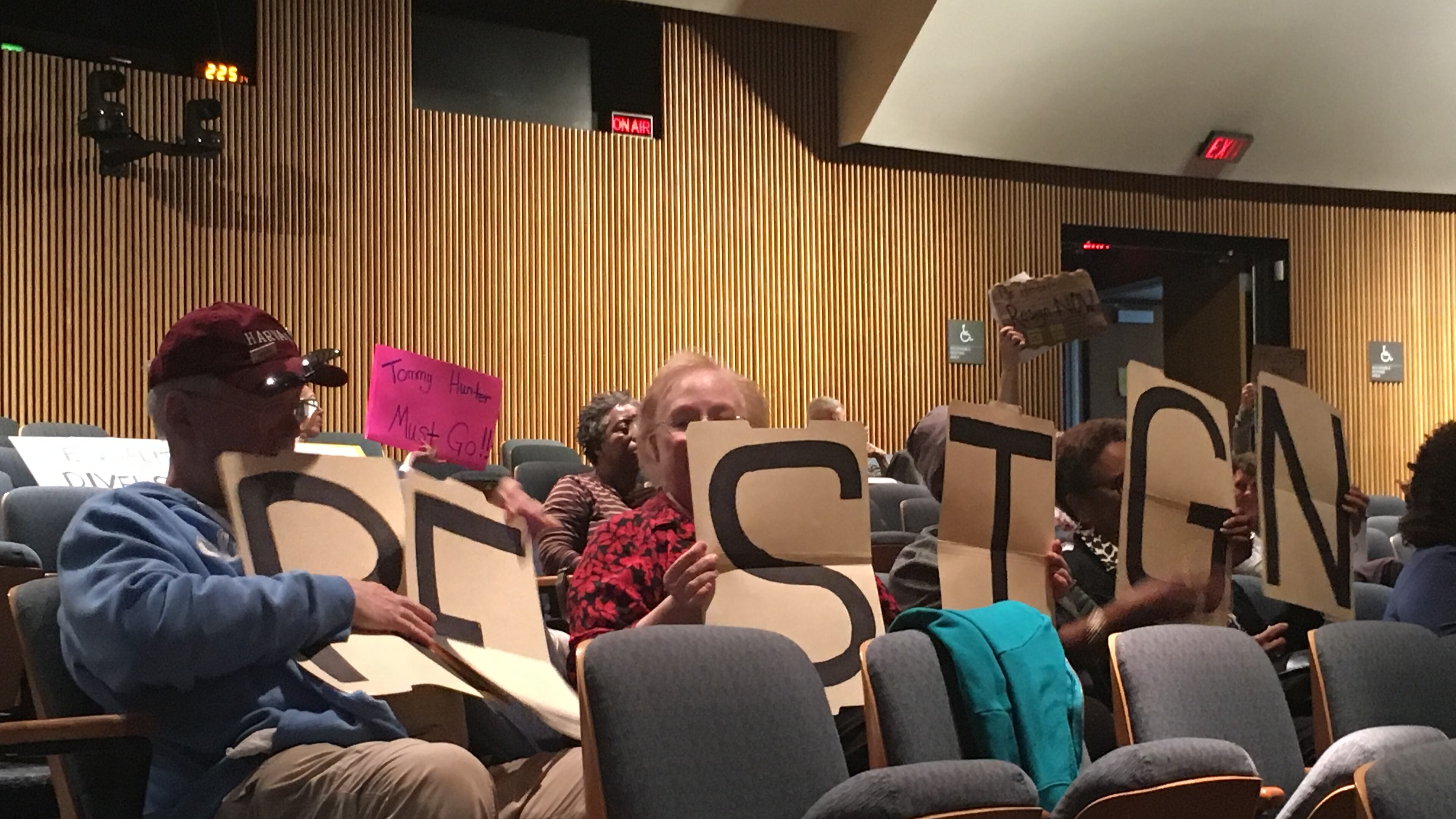 A group of protesters holds signs urging Gwinnett County Commissioner Tommy Hunter to resign during a Board of Commissioners meeting on Feb. 21.