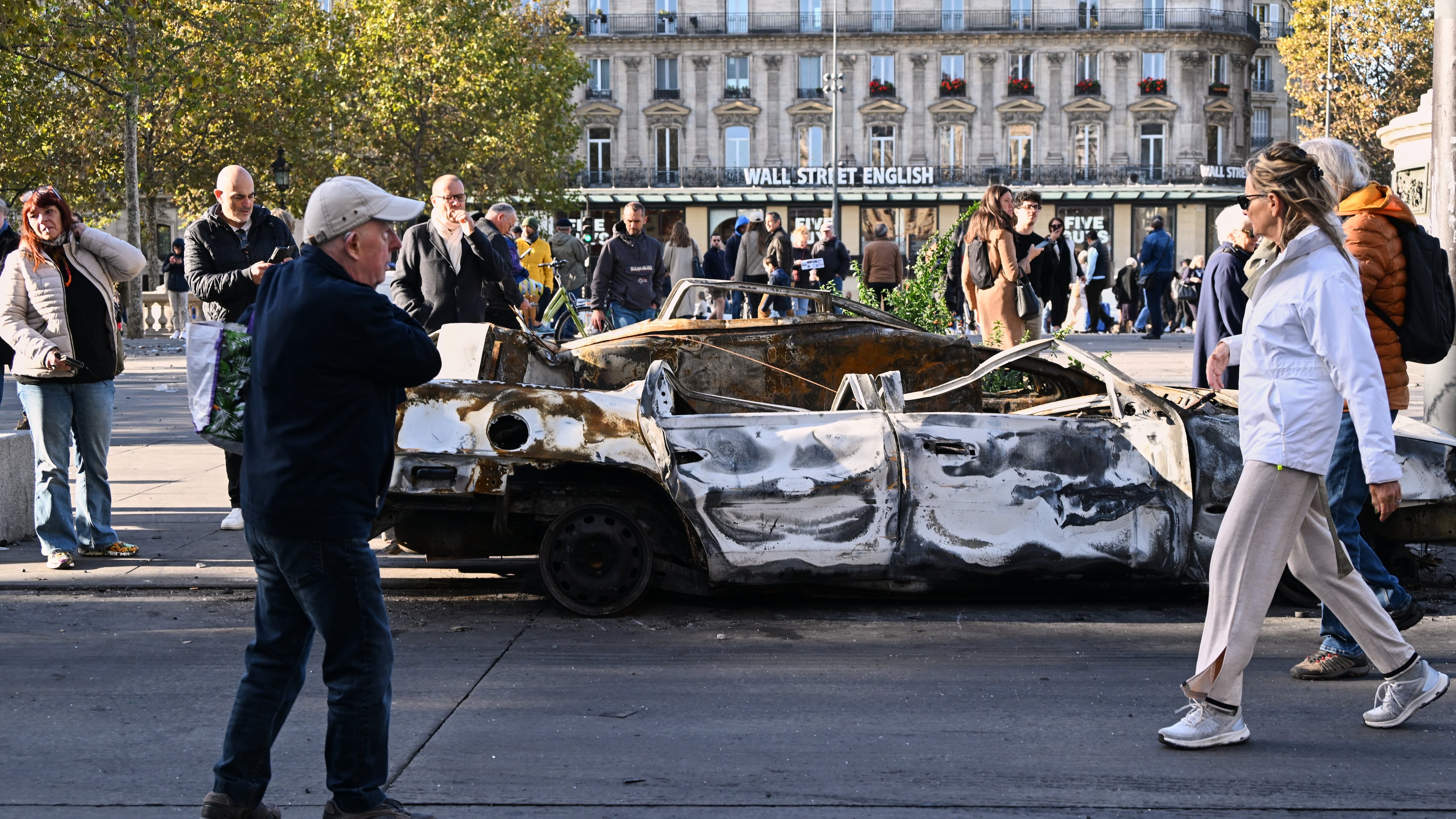 People look at a charred car on Place de la Republique the day after a demonstration against rising living costs, joining students' grievances, in Paris, Sunday, Oct. 18, 2026. (AP Photo/Emma Da Silva)