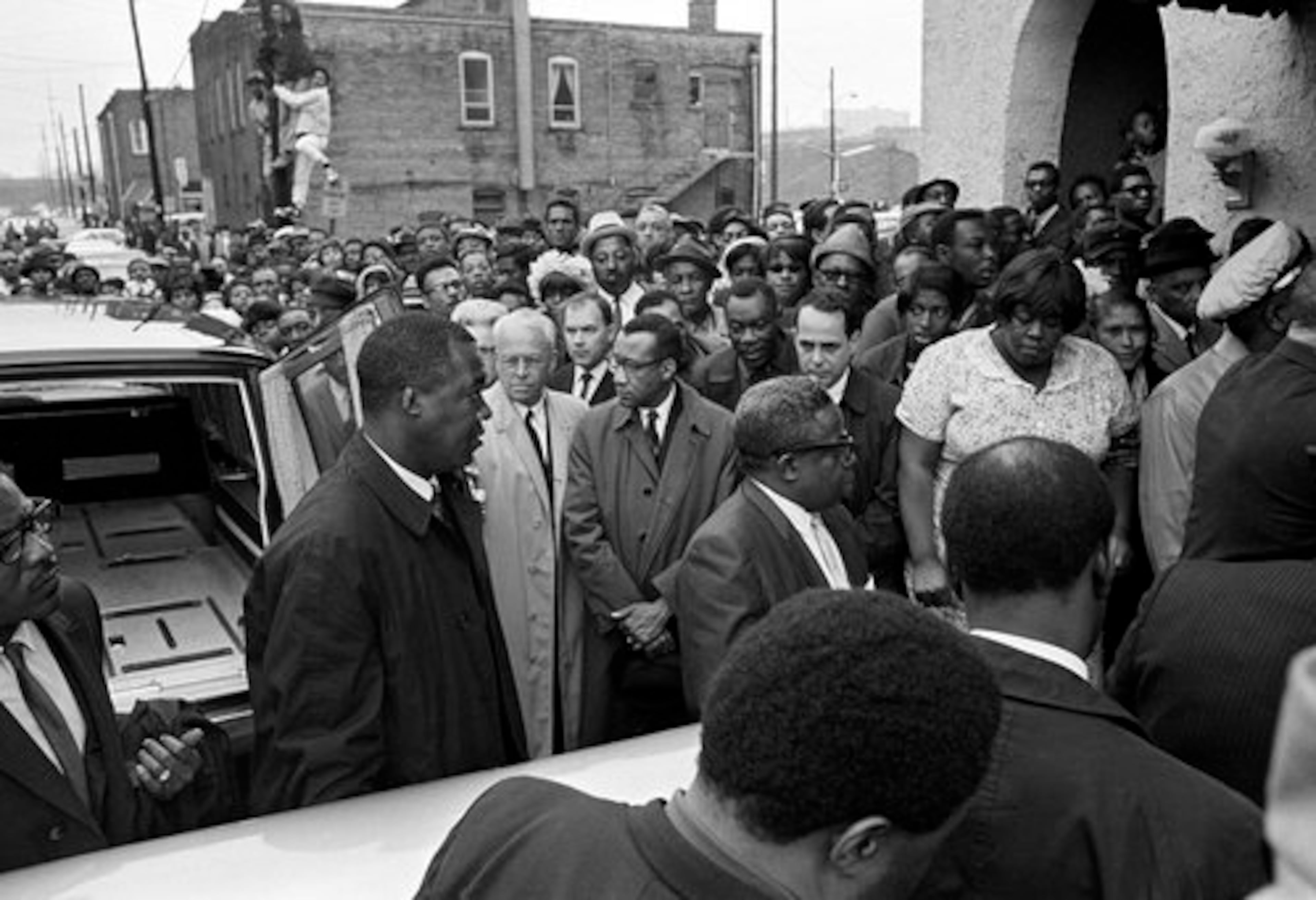Crowds gather outside a funeral home as the casket holding the body of Dr. Rev. Martin Luther King Jr., is carried inside in Atlanta, Ga., April 5, 1968 The man standing at center, near rear door of hearse, is Atlanta Mayor Ivan Allen; next to the mayor is Moneta Sleet Jr. When Mrs. Coretta Scott King learned that the pool of photographers covering the funeral did not include a black photographer, she sent word that if Mr. Sleet were not allowed in the church, there would be no photographers.