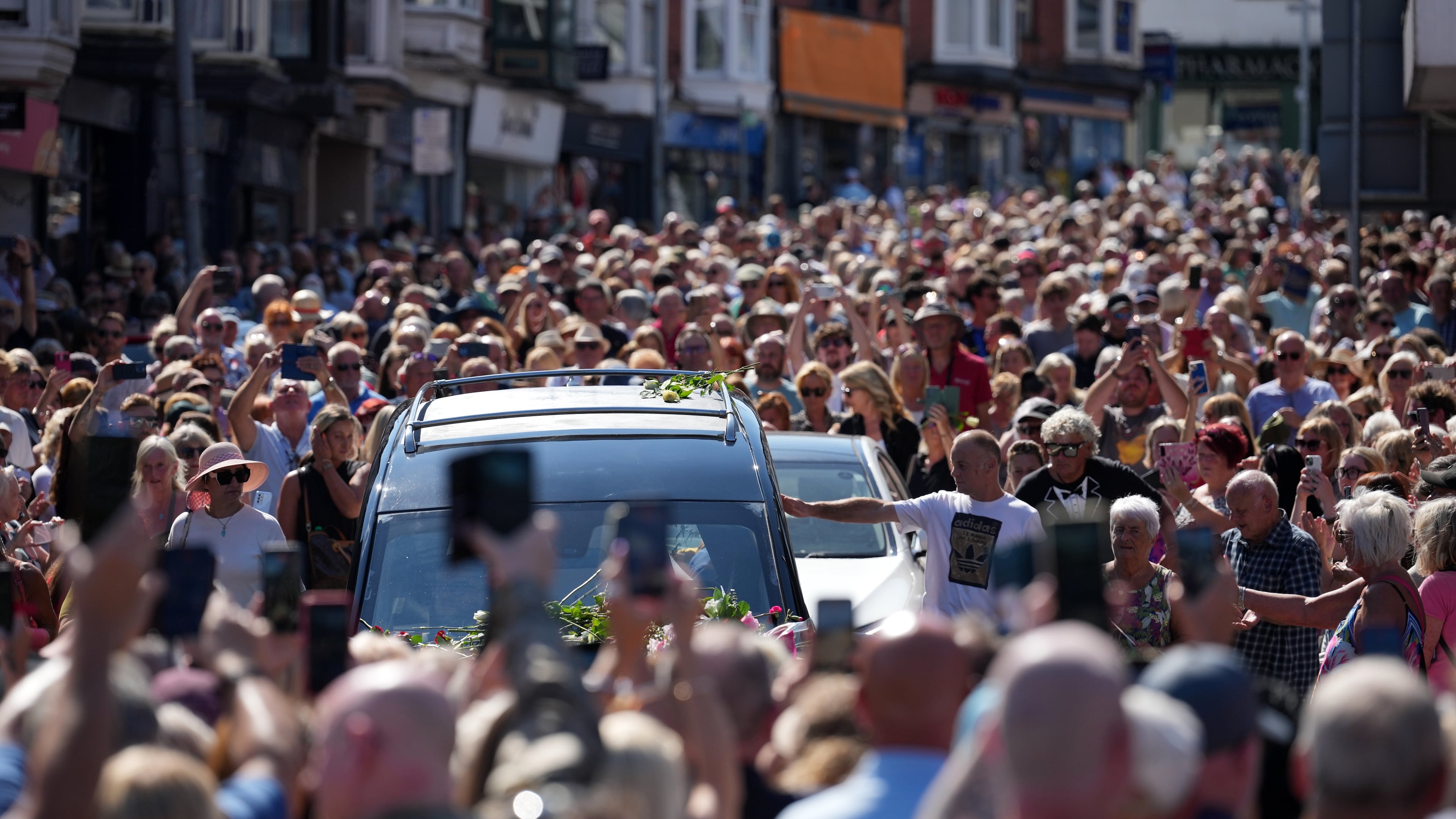 Fans of singer Bonnie Tyler line the streets as her coffin is transported in a hearse back to her former home ahead of her funeral, in Mumbles, Wales, Saturday, Aug. 15, 2026. The Total Eclipse Of The Heart musician, whose real name was Gaynor Hopkins, died in hospital in Portugal on July 8 at the age of 75. (AP Photo/Alastair Grant)