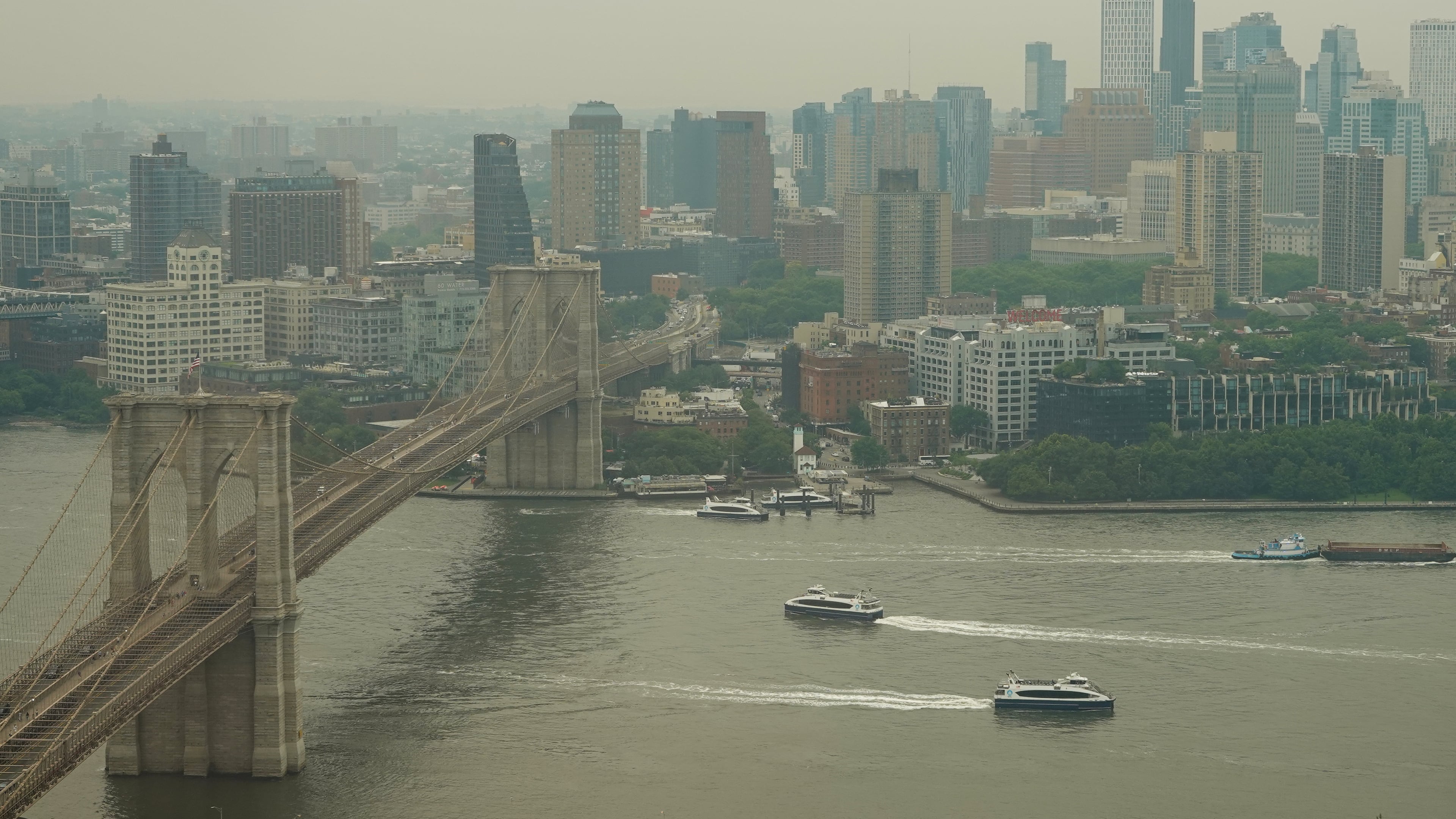 Boats maneuver the East River near the Brooklyn Bridge as smoke from wildfires blankets the sky Thursday, July 16, 2026, in New York. (AP Photo/Alyssa Goodman)