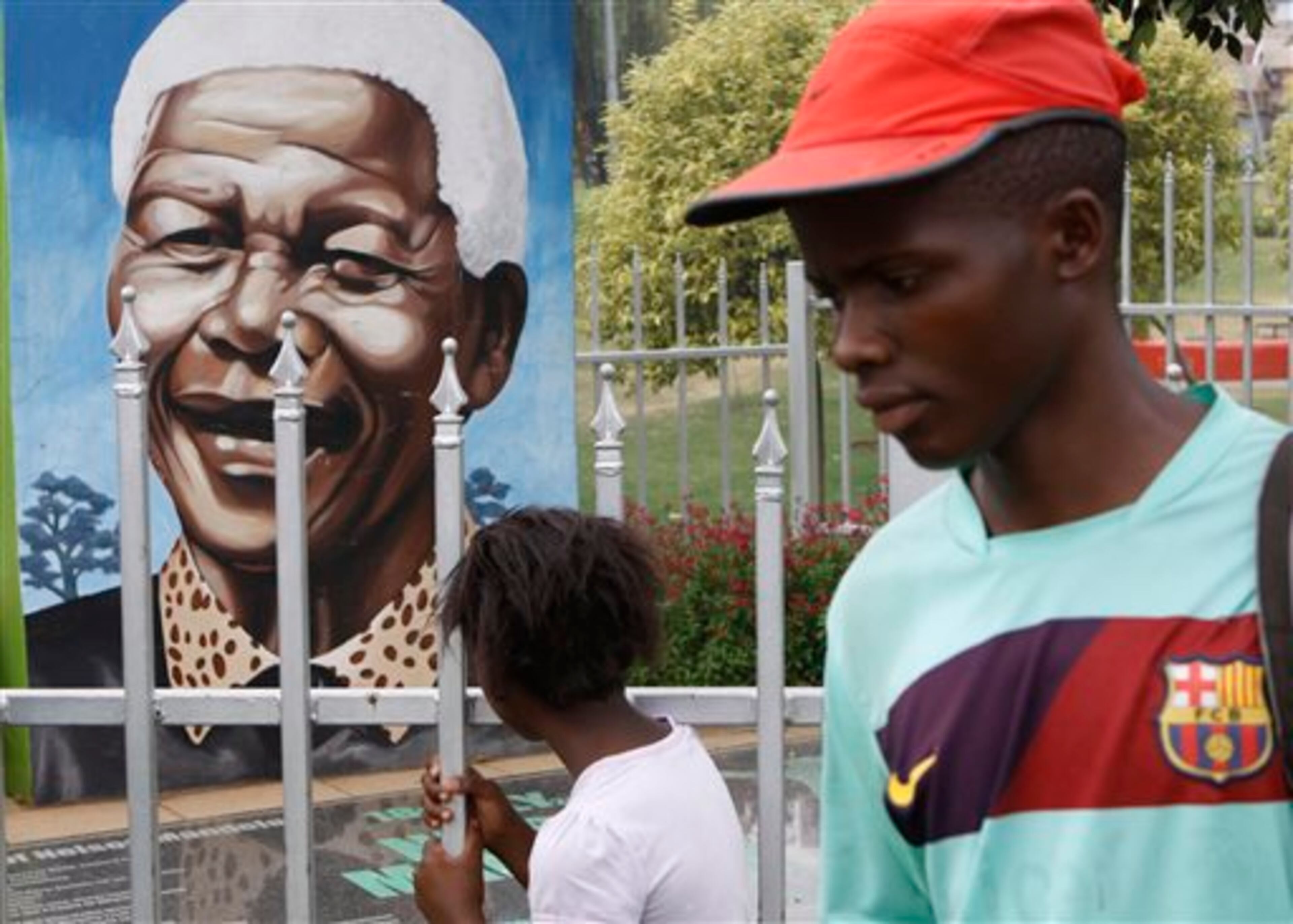 FILE - A child looks through a fence at a portrait of former President Nelson Mandela in a park in Soweto, South Africa, in this March 28, 2013 file photo. The Nobel laureate is a revered figure in South Africa, which has honored his legacy of reconciliation by naming buildings and other places after him and printing his image on national banknotes. On Thursday, Dec. 5, 2013, Mandela died at the age of 95. (AP Photo/Denis Farrell, File)
