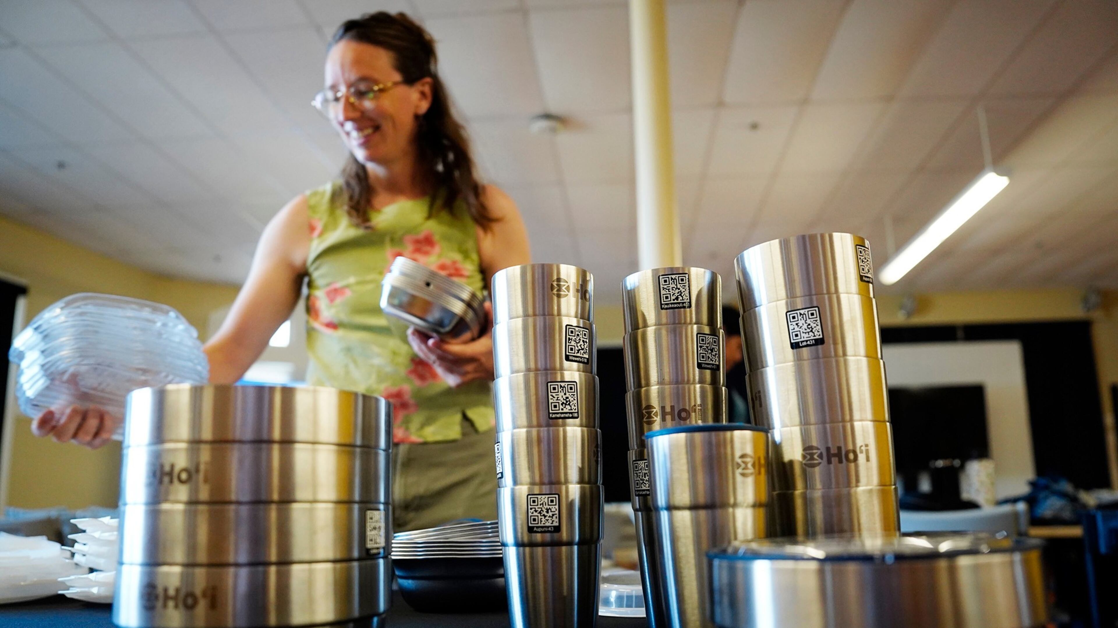 Bethany Letoto, business development lead at Ho'i, a returnable dish program, sets out the re-useable containers before an open house on Tuesday, June 30, 2026, in Hilo, Hawaii. (Kevin Fujii/Honolulu Civil Beat via AP)