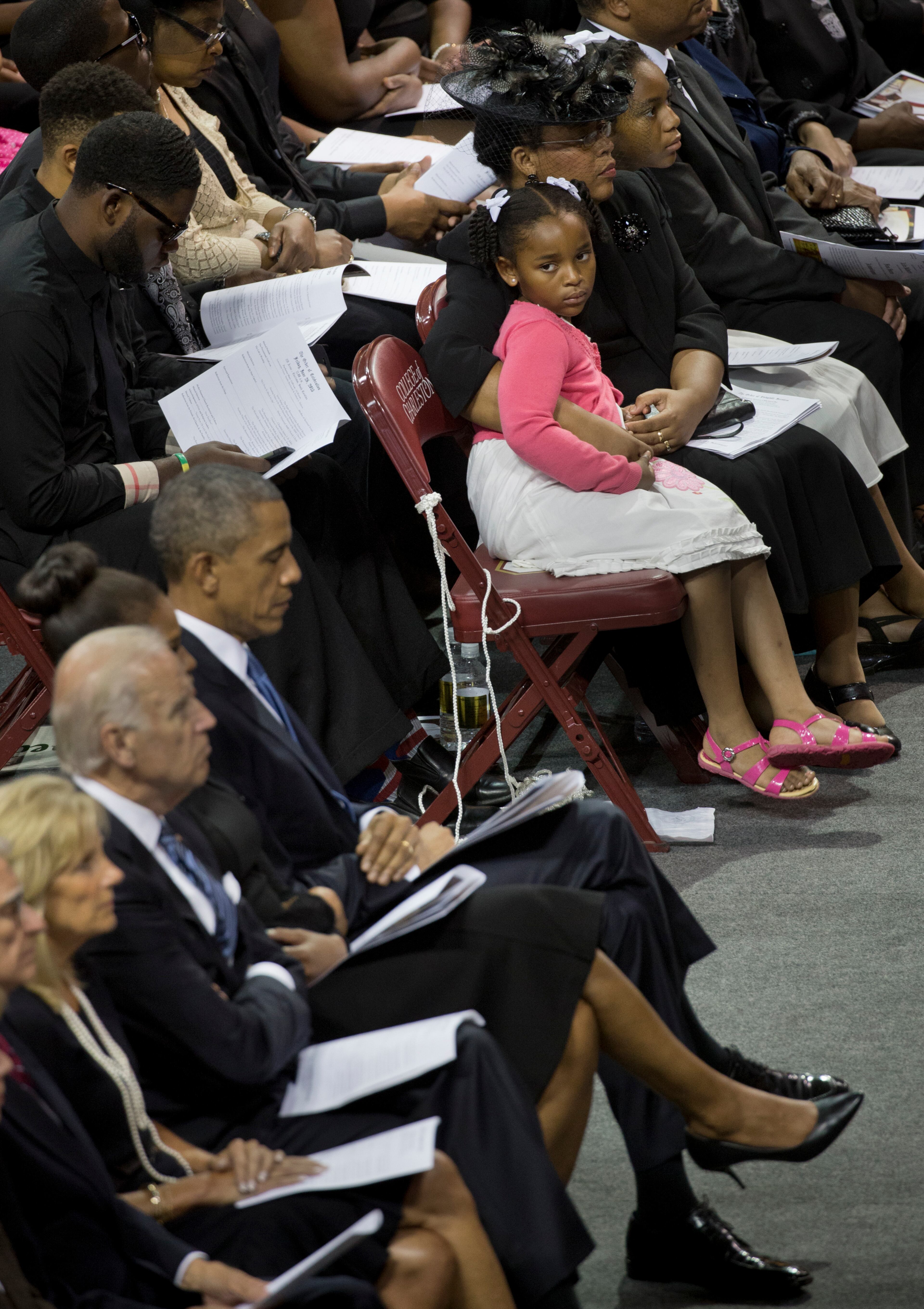 Malana Pinckney, a daughter of the late Rev. Clementa Pinckney, looks to President Barack Obama during a funeral service for her father, at the TD Arena in Charleston, S.C., June 26, 2015. Obama was on hand to eulogize Pinckney, a state senator and pastor who was shot dead along with eight other black churchgoers at his church in Charleston. Front row from top: Eliana Pinckney, Jennifer Pinckney, Malana Pinckney, Obama, Michelle Obama, Joe Biden, Jill Biden. (Stephen Crowley/The New York Times)