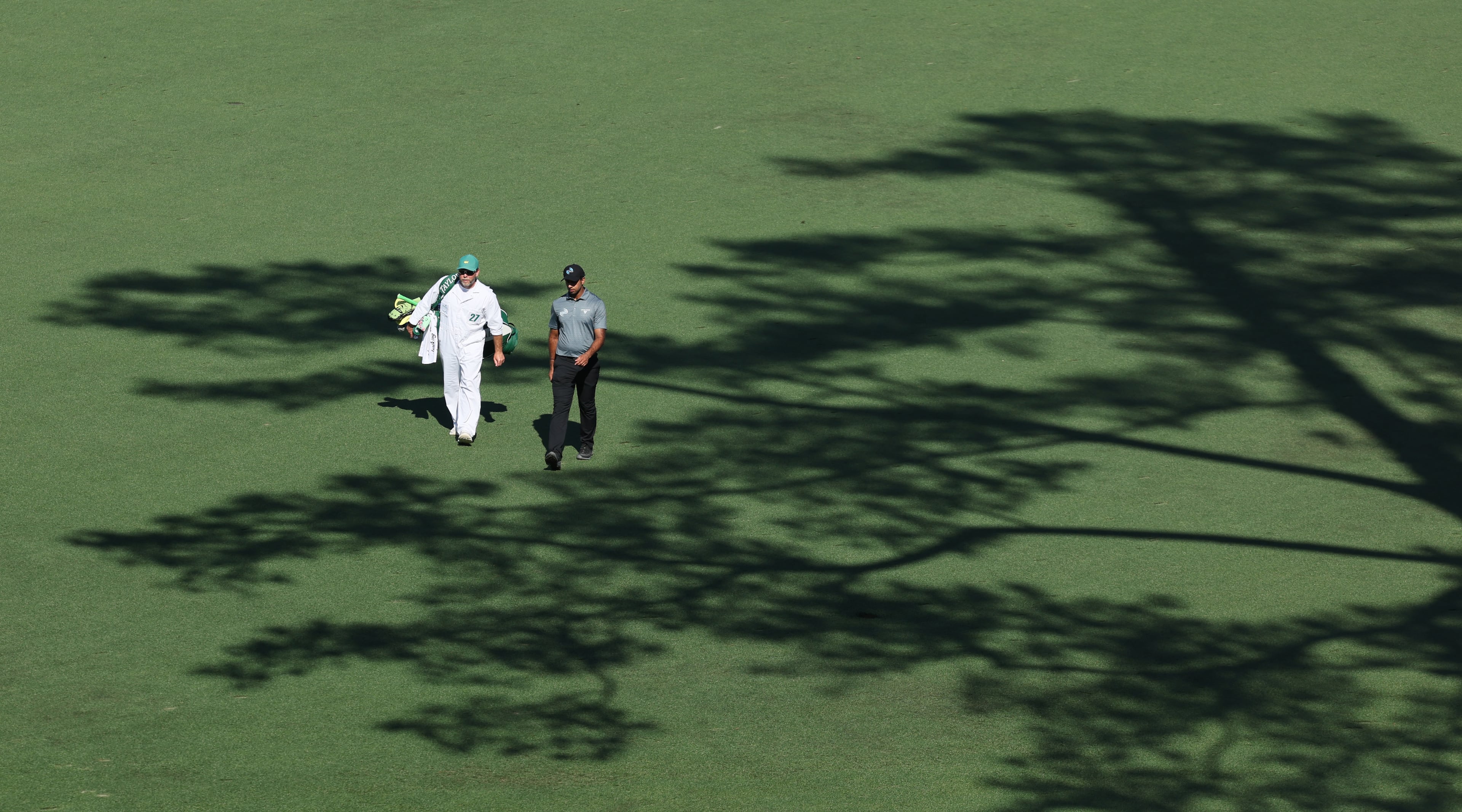 Aaron Rai and caddie Jason Timmis walk down the 15th fairway through the shadow of a pine tree during first round of the Masters Tournament, at Augusta National Golf Club, Thursday, April 9, 2026, in Augusta, Ga. (Jason Getz/AJC)