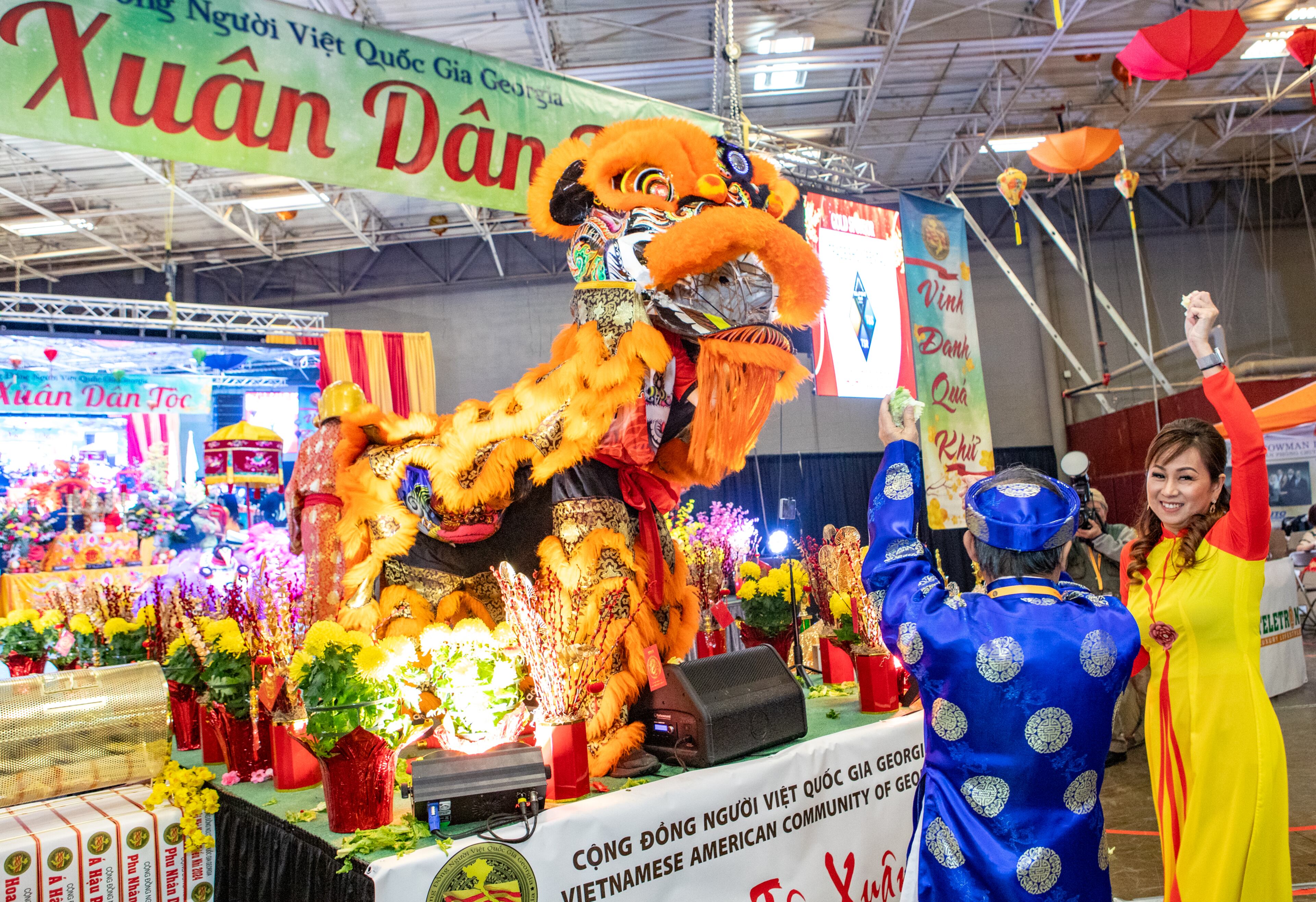 During the lion dance performance, Hieu Le, in blue and Tramy Nguyen, right, catch a vegetable thrown out by the lion during the Lunar New Year celebration at Plaza Las Americas in Lilburn on Saturday, Feb 3, 2024 where dragon and lion dancing begins the weekend. The celebration continues on Sunday and includes traditional food, music and cultural festivities. (Jenni Girtman for The Atlanta Journal-Constitution)