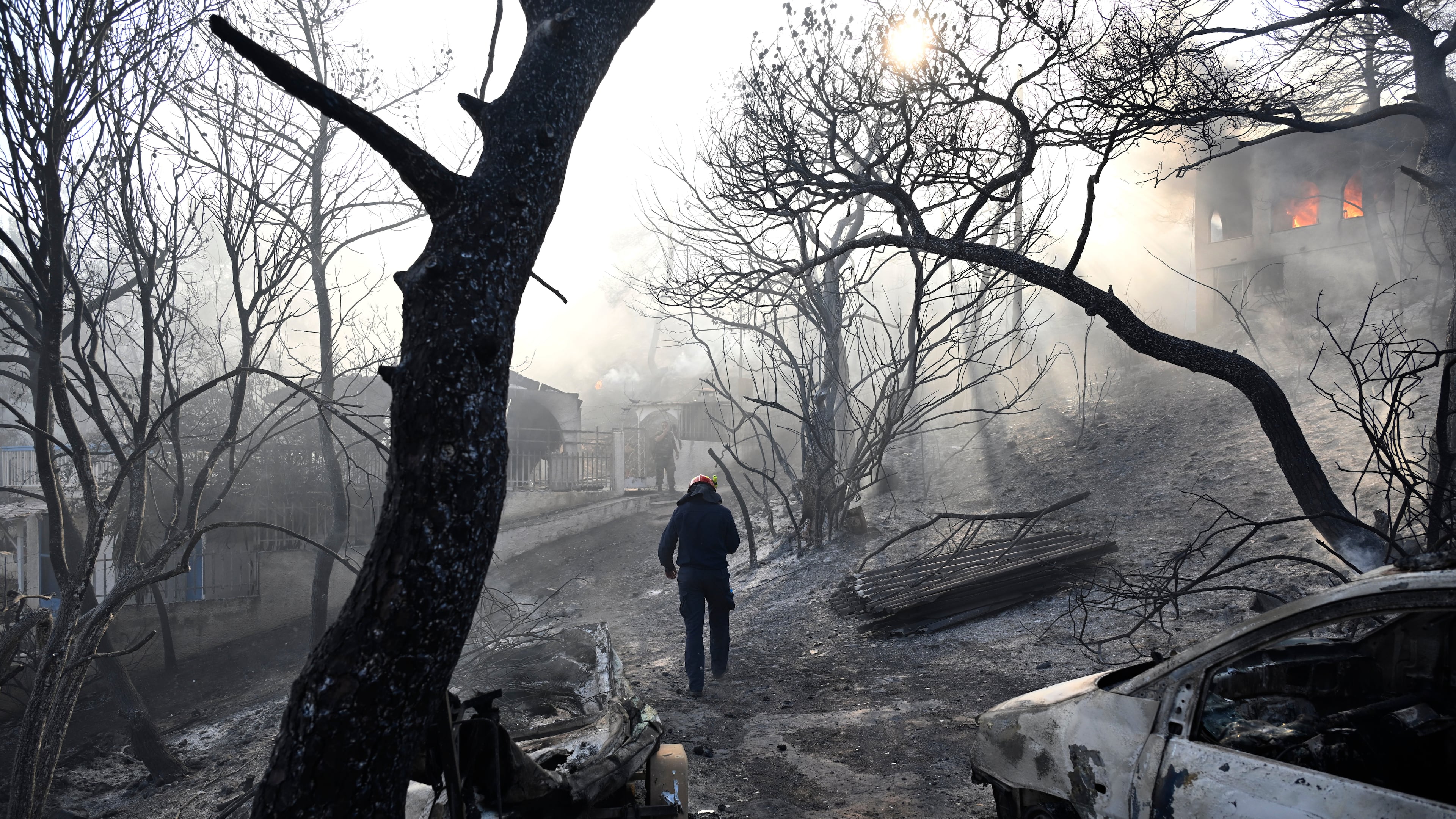 A firefighter walks through a burned area as flames engulf a house during a wildfire on the island of Salamina, west of Athens, Greece, Sunday, Aug. 16, 2026. (AP Photo/Michael Varaklas)