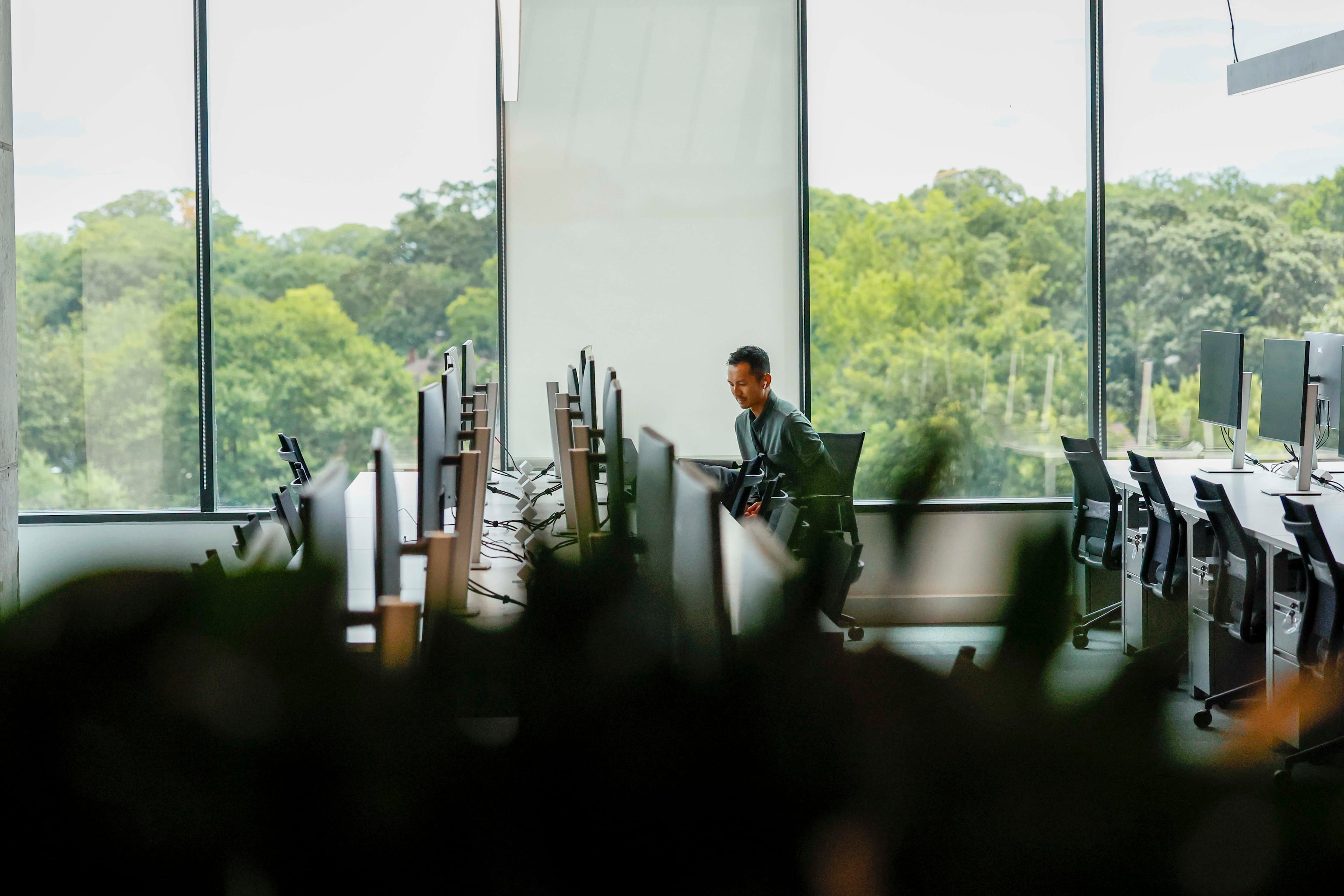 A Rivian employee is seen working near large windows overlooking the Atlanta Beltline Eastside Trail at Rivian’s new East Coast headquarters. (Miguel Martinez/AJC)