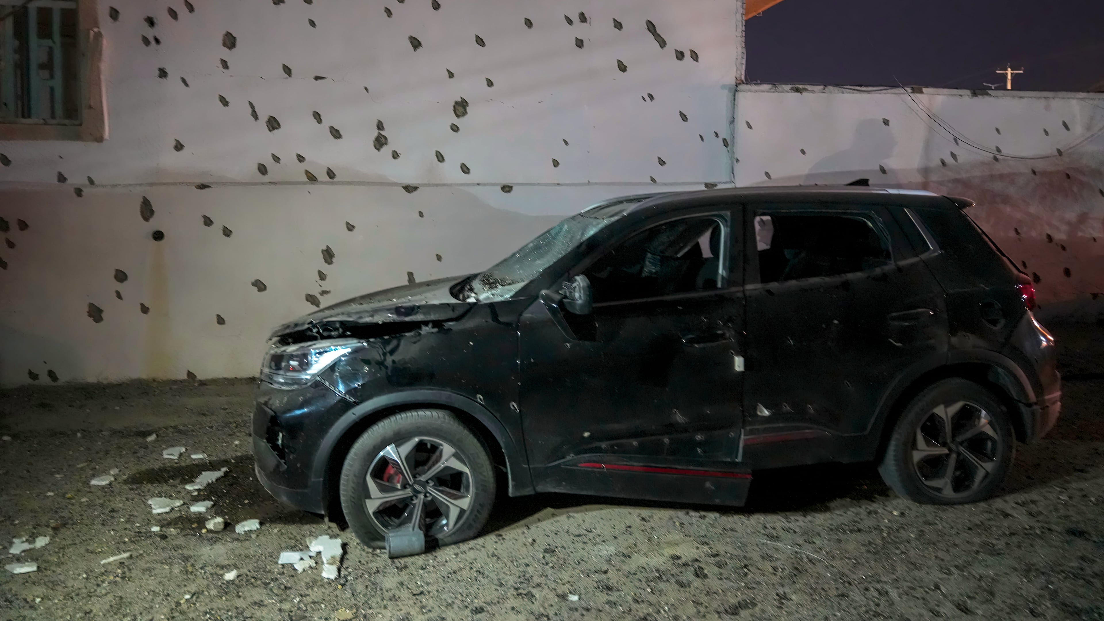 A damaged car sits beside a wall bearing numerous impact marks near the site of a strike in Lamerd, southern Iran, Saturday, Feb. 28, 2026. (Alireza Ameri/Tasnim News Agency via AP)