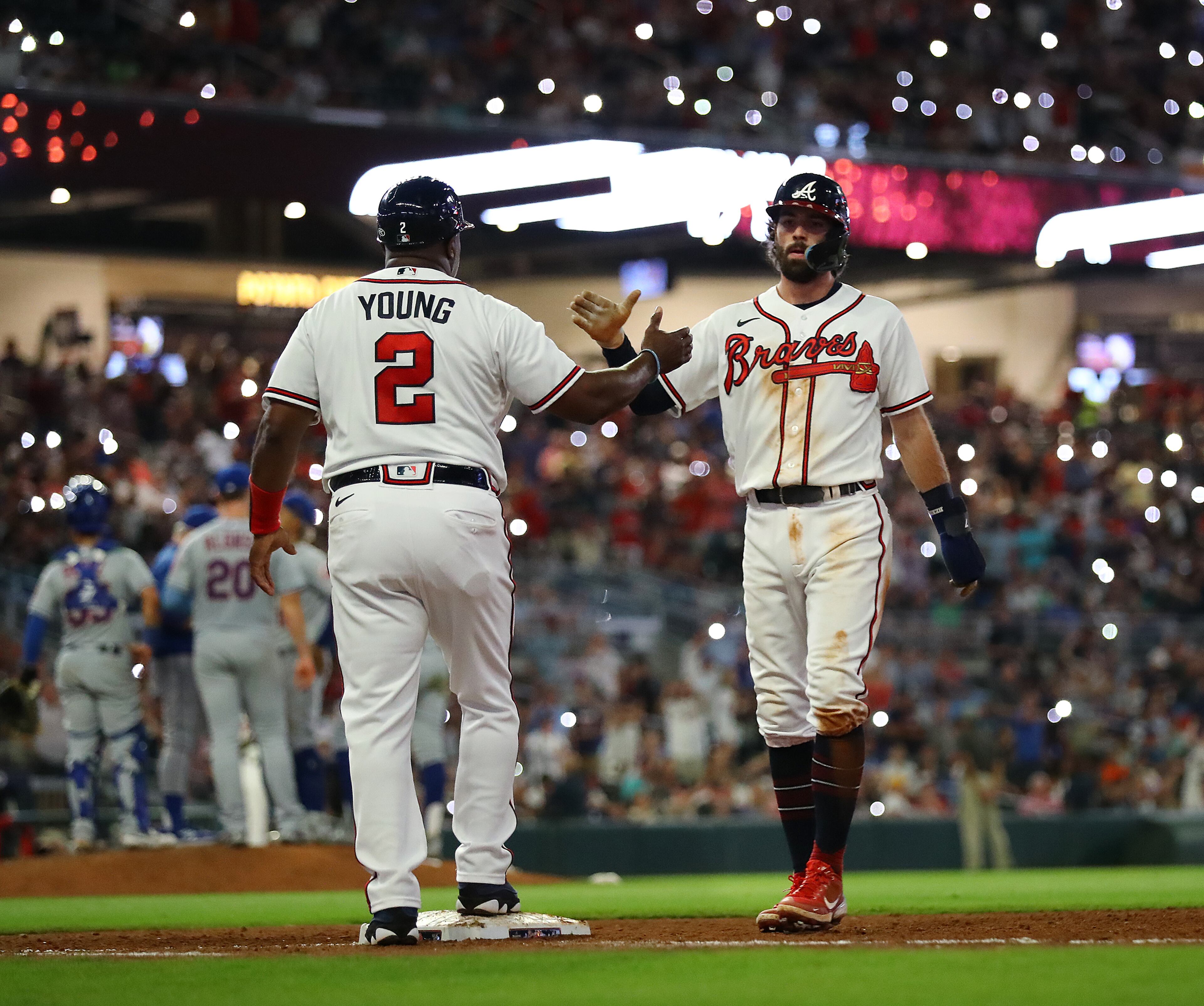 Braves shortstop Dansby Swanson gets five from first base coach Eric Young with the lights turned out while the New York Mets change pitchers after his RBI-single to score outfielder Ronald Acuna for a 4-0 lead over the Mets during the seventh inning in a MLB baseball game on Tuesday, August 16, 2022, in Atlanta. The Braves shut out the Mets 5-0. “Curtis Compton / Curtis Compton@ajc.com