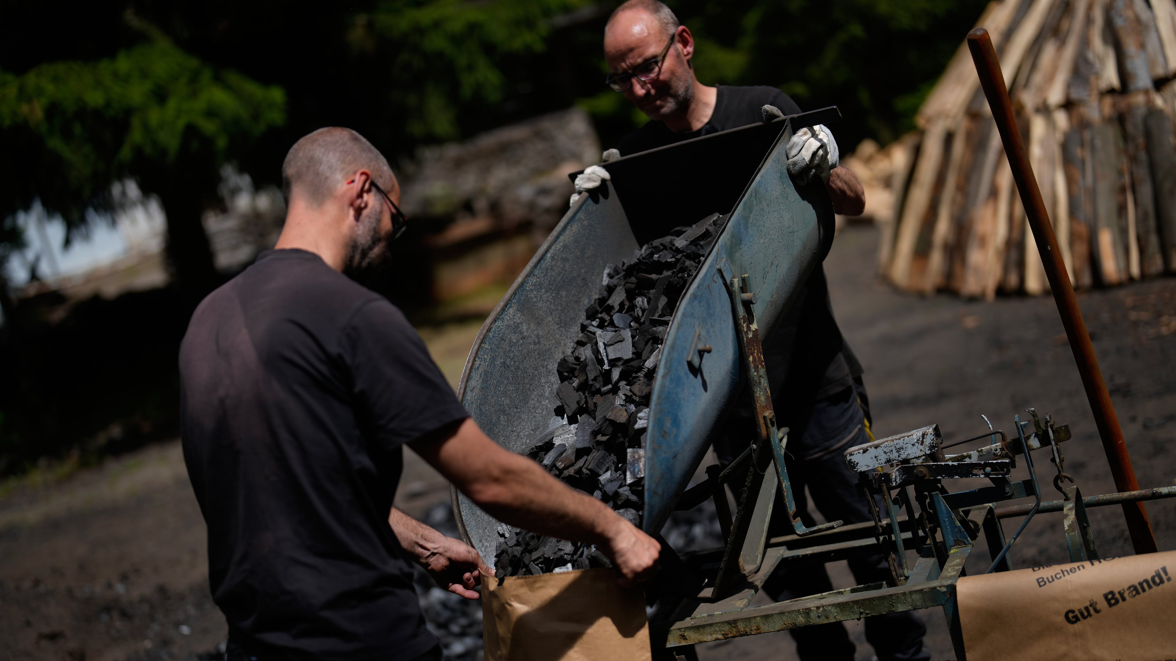 Brothers Immo and Sascha Feldmer put charcoal into paper bags after weighing it at their traditional production site near Hasselfelde in Germany's Harz, Germany, Thursday, June 18, 2026. (AP Photo/Matthias Schrader)