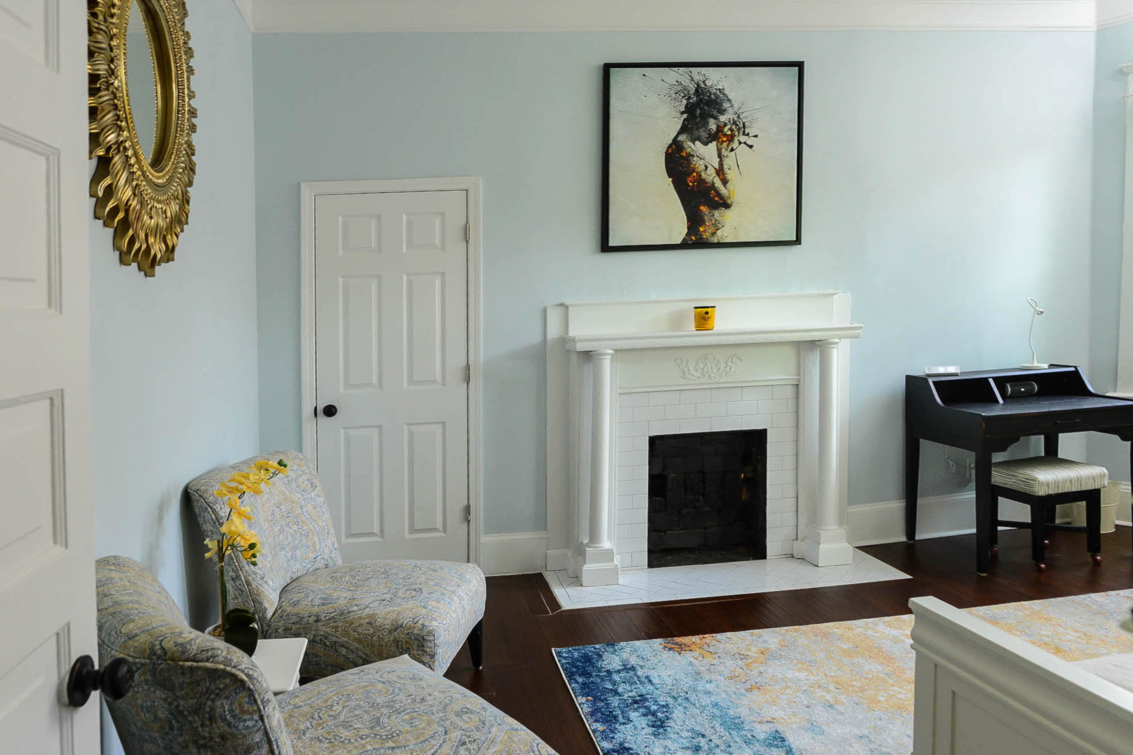 Deliberation by Mario Sánchez Nevado hangs above one of the home's three coal fireplaces. The pair of chairs, which they reupholstered material from Fine Fabrics, and sunburst mirror were free through Facebook Marketplace.