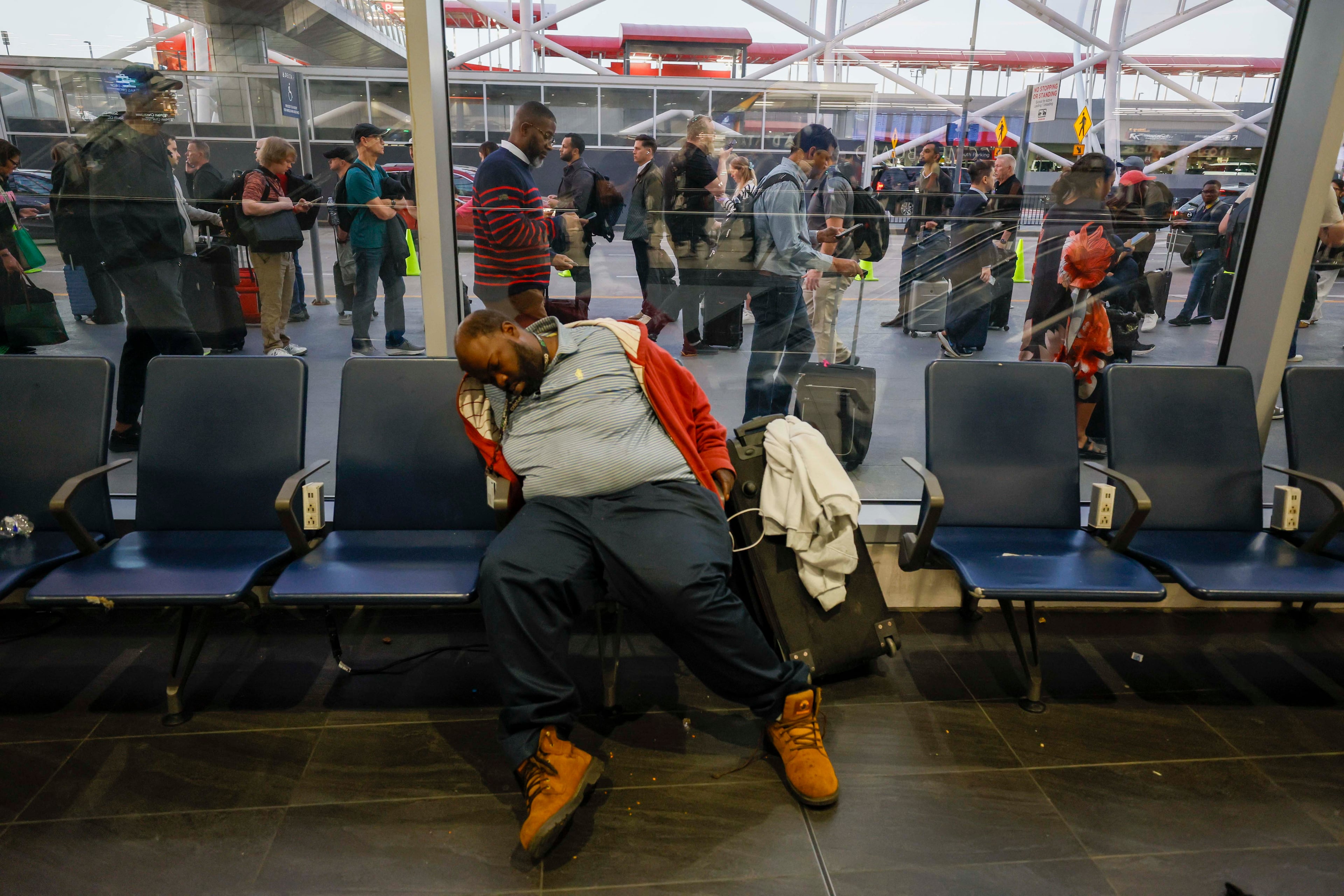 A traveler peacefully sleeps as people start walking along the airport sidewalk for TSA security checks early in the morning of March 23 at Hartsfield-Jackson Atlanta International Airport during the partial government shutdown. (Miguel Martinez/AJC)