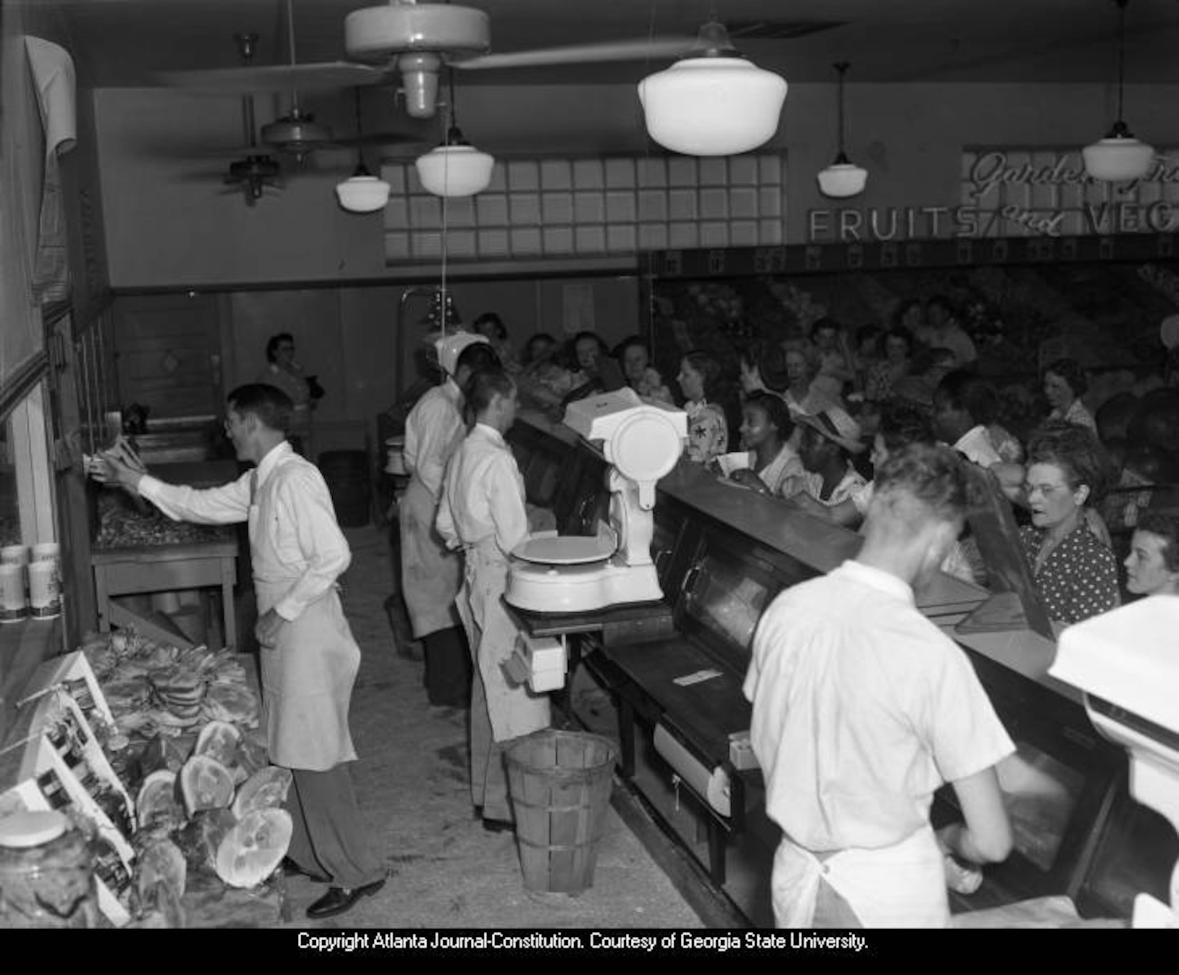 Deli workers behind a counter take orders from a large group of grocery shoppers on July 21, 1946.