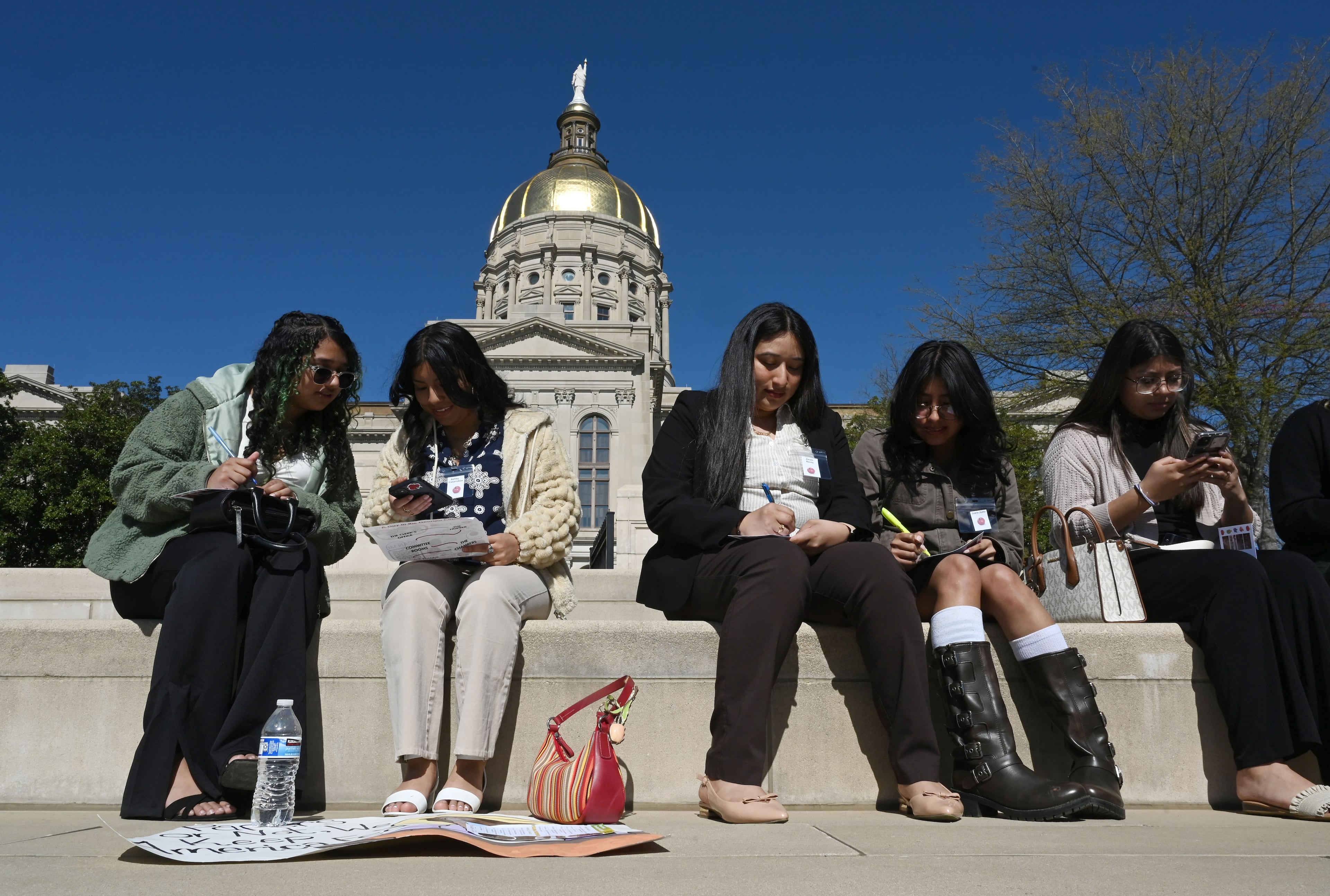 Participating students (from left) Alexis Gonzalez, Ashley Casarrubias, Juana Justo and Josie Fountain write a letter on a postcard to deliver their messages to their representatives in Liberty Plaza ahead of visiting the Georgia State Capitol, Friday, March 21, 2025, in Atlanta. Organized for the fifth consecutive year by the Atlanta-based Latino Community Fund Georgia, the “Farmworker Families at the Capitol” event is meant to bridge the gap between remote rural communities and the state’s center of political power. (Hyosub Shin/AJC)