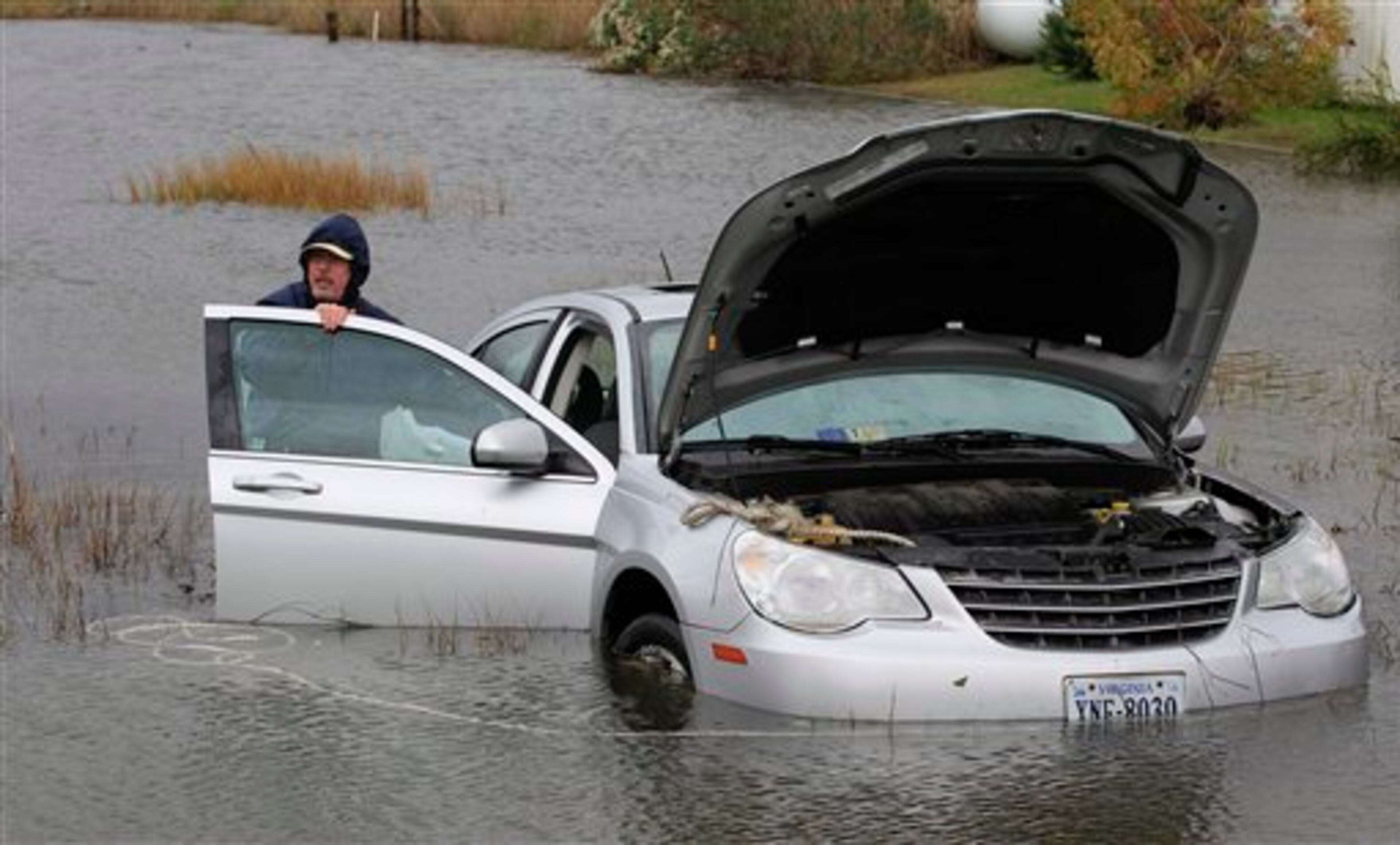 Glenn Heartley works on his car in a creek in Chincoteague, Va., Tuesday, Oct. 30, 2012. Heartley and his wife were swept off the road into a shallow creek when superstorm Sandy struck the area Monday. (AP Photo/Steve Helber)