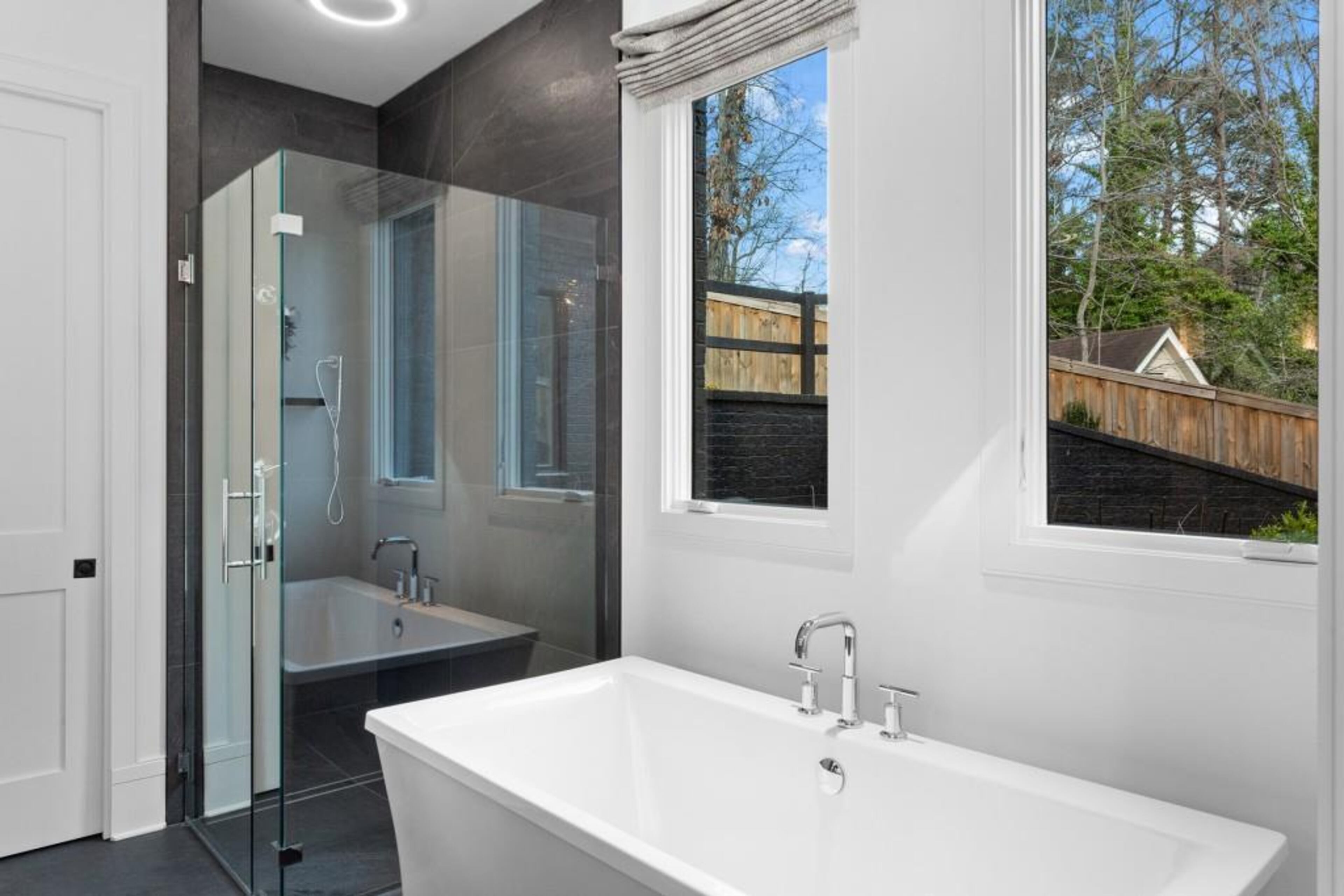 Oversized primary suite on main features 15-plus foot ceilings and spa bath featuring double vanity, soaking tub, frameless shower, and custom closet.