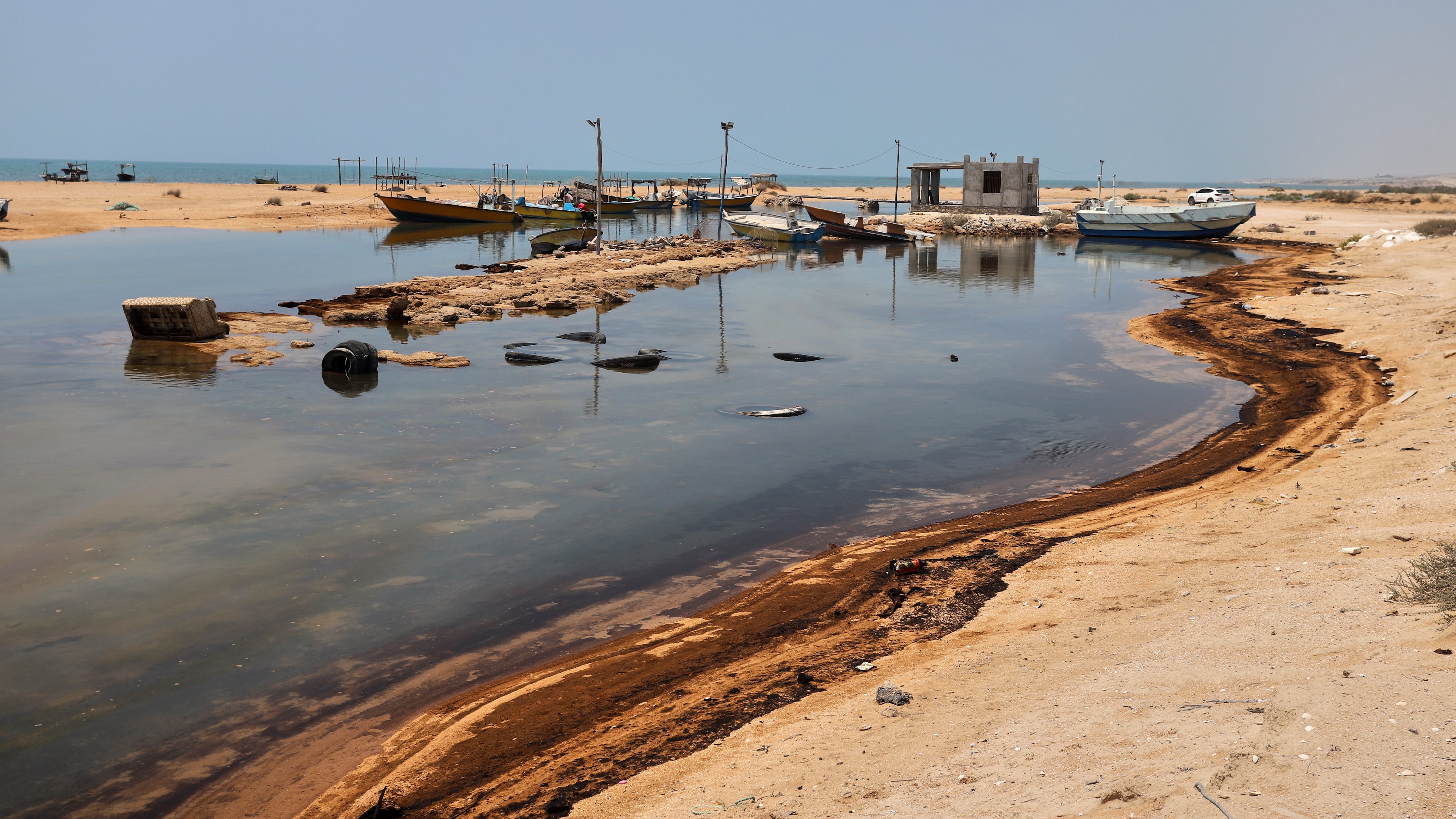 Oil residue lines the shore near fishing boats on Qeshm Island, Iran, Thursday, Aug. 13, 2026, amid ongoing wartime attacks on vessels and infrastructure in and around the Strait of Hormuz, though the spill's source has not been independently determined.(Amirhosein Khorgooi/ISNA via AP)