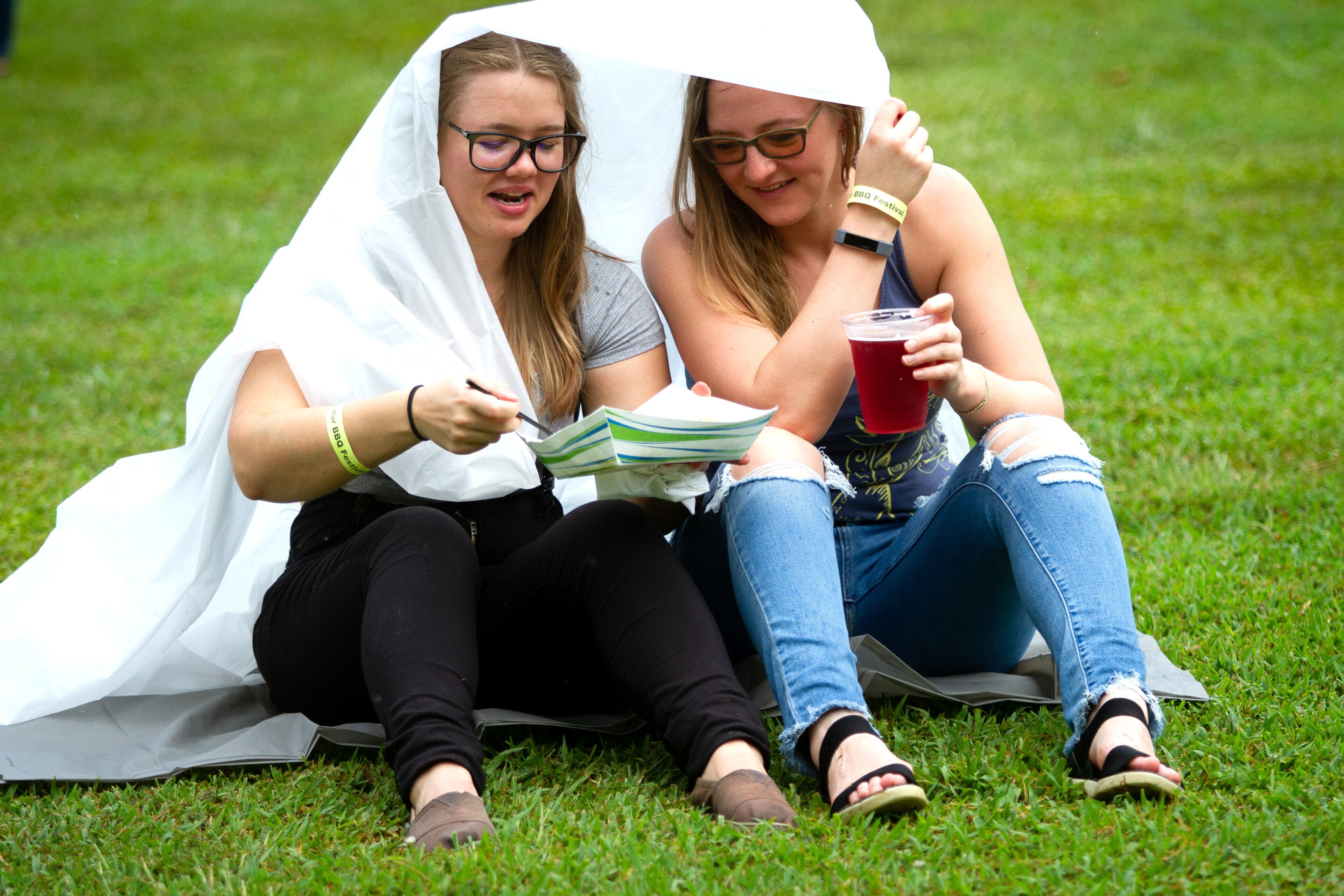 Aley McLellan (L) and her sister Katie McLellan try to stay dry during a short rain shower at the 19th annual Decatur BBQ Blues & Bluegrass festival on Saturday, August 10, 2019. STEVE SCHAEFER / SPECIAL TO THE AJC