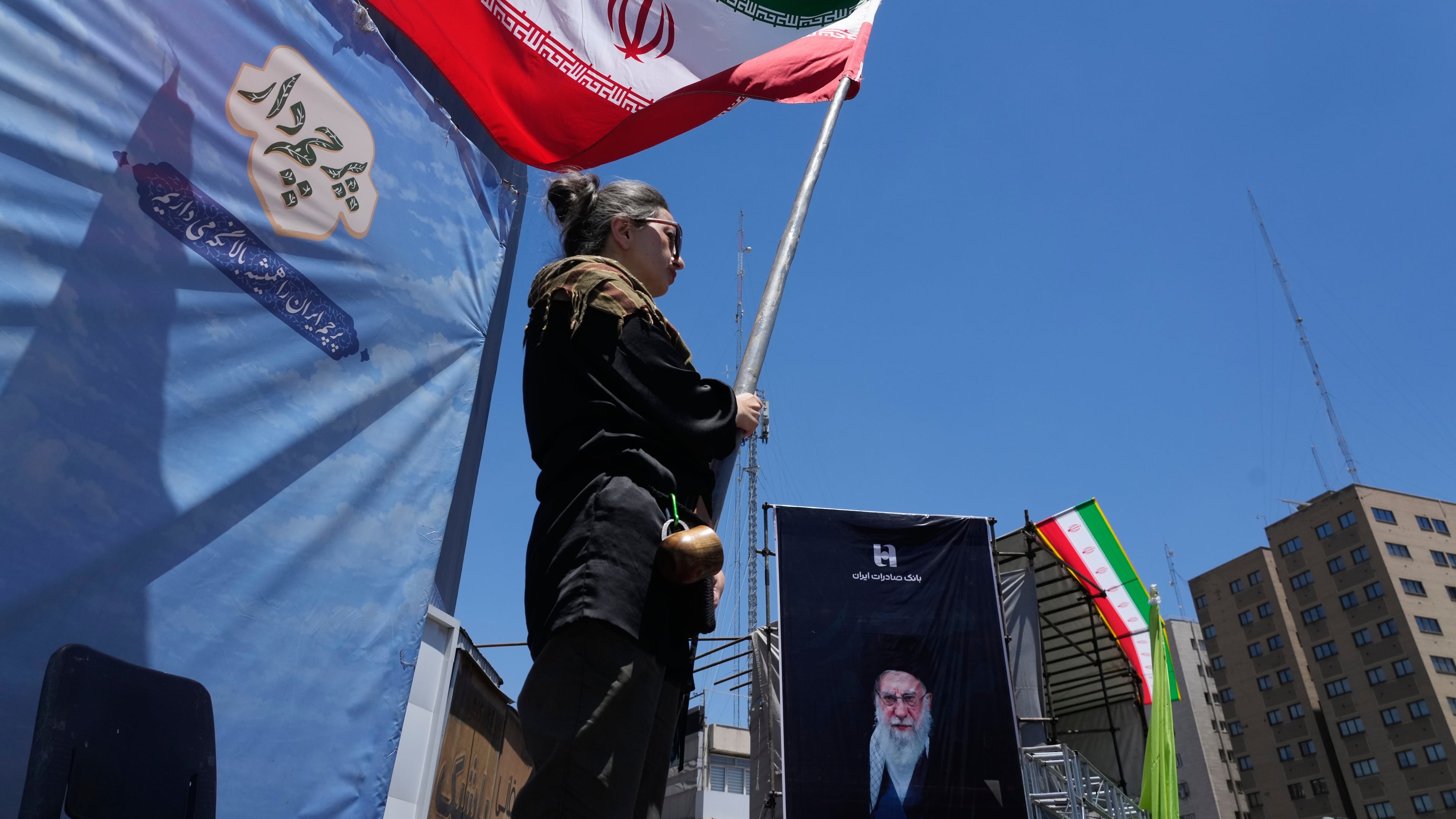 A woman waves an Iranian flag during a pro-government campaign as a portrait of the slain Supreme Leader Ayatollah Ali Khamenei, who was killed in U.S. and Israeli strikes on Feb. 28, is displayed at right, in downtown Tehran, Iran, Monday, June 15, 2026. (AP Photo/Vahid Salemi)