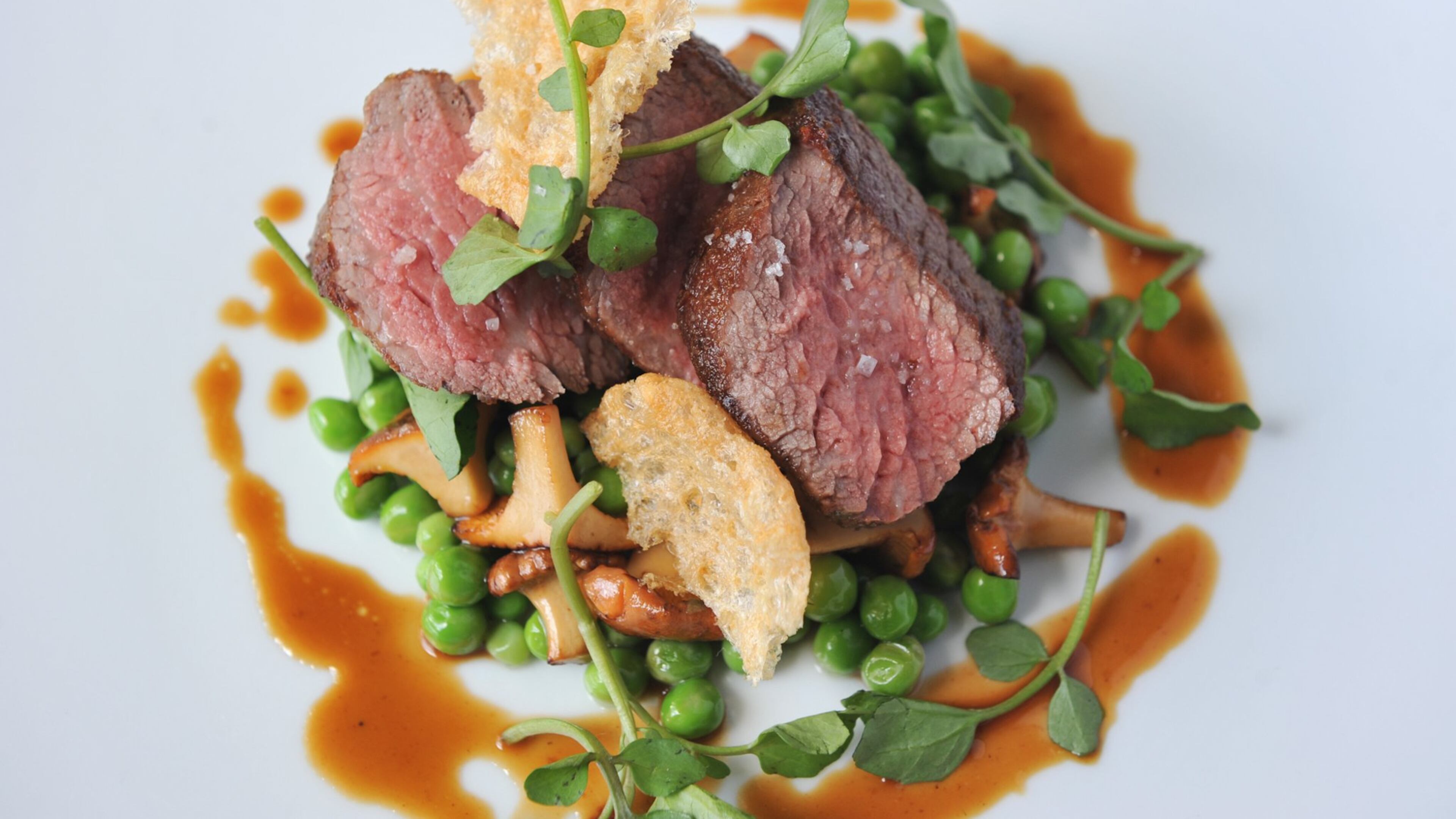 Dry-aged rib-eye is served with English peas, chanterelle mushrooms, puffed beef tendon and wild watercress at Five and Ten in Athens. (Becky Stein)