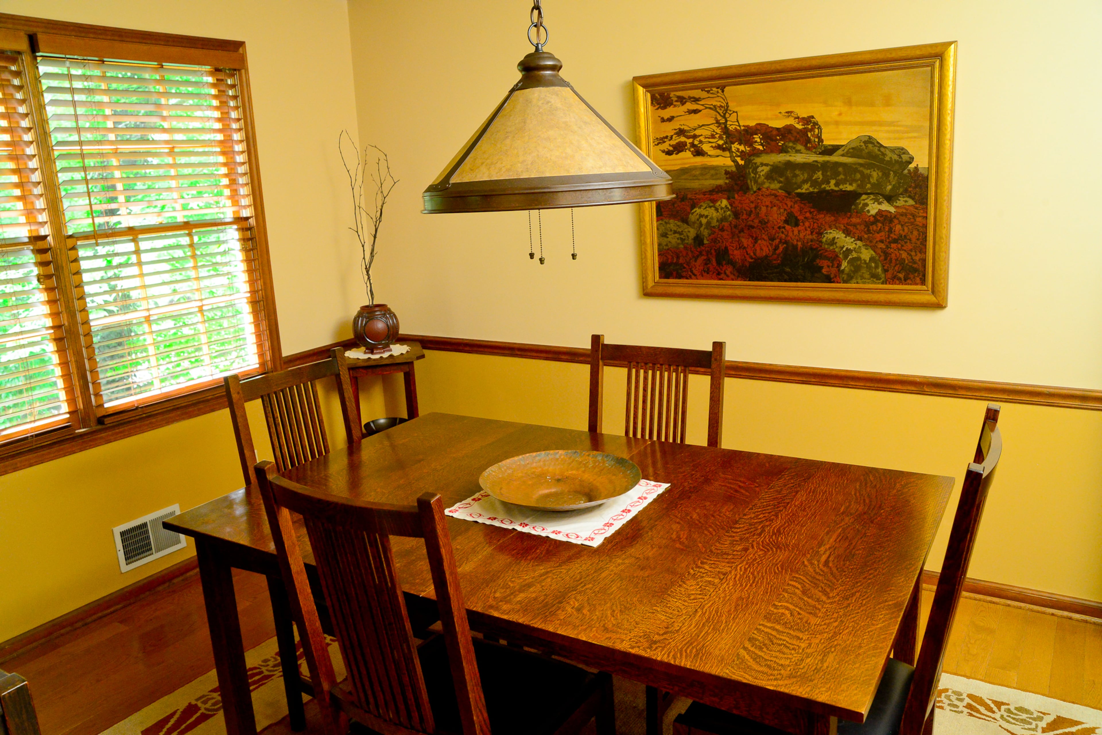 The dining room's walls are painted Sherwin-Williams' "Buckram Binding" above the chair rail and "Empire Gold" below. The dining table and chairs are reissued L&JG Stickley items, with a hammered copper bowl as the centerpiece. The Tibetan rug is a new item, made by Tiger Rug Co.