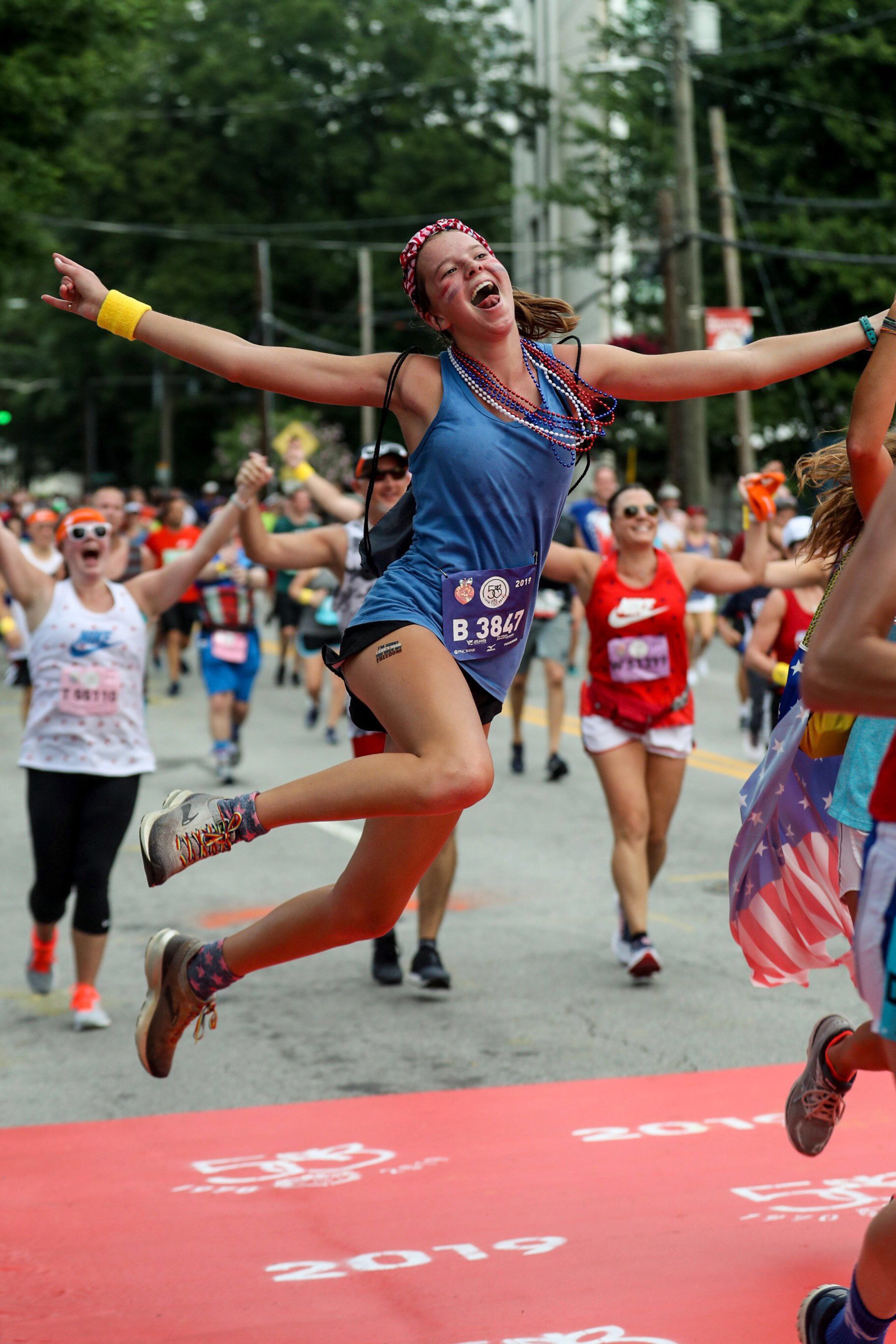 Atlanta, Georgia -- A runner jumps in celebration as she nears the finish line during the AJC Peachtree Road Race in Atlanta, Thursday, July 4, 2019. (Alyssa Pointer/alyssa.pointer@ajc.com)