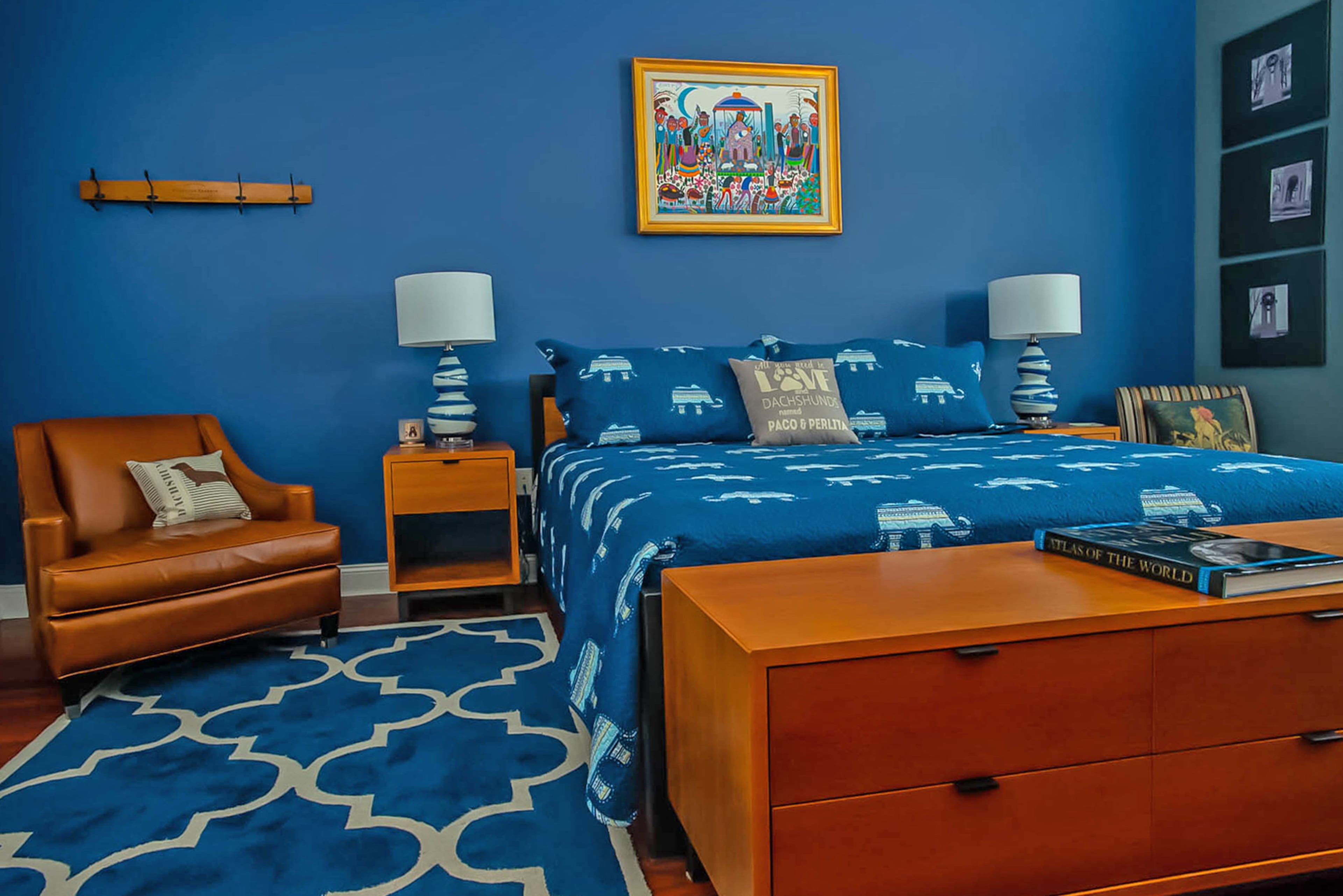 The master bedroom is awash in blue. The bedroom suite, which has a cherry finish, is from the Copenhagen collection by Room & Board. The pillows are a fun nod to Larry Henderlight and Julio Gomez's pets. The painting, titled "Nacimiento" is by a Hispanic artist and depicts the nativity. Christopher Oquendo/AJC FILE