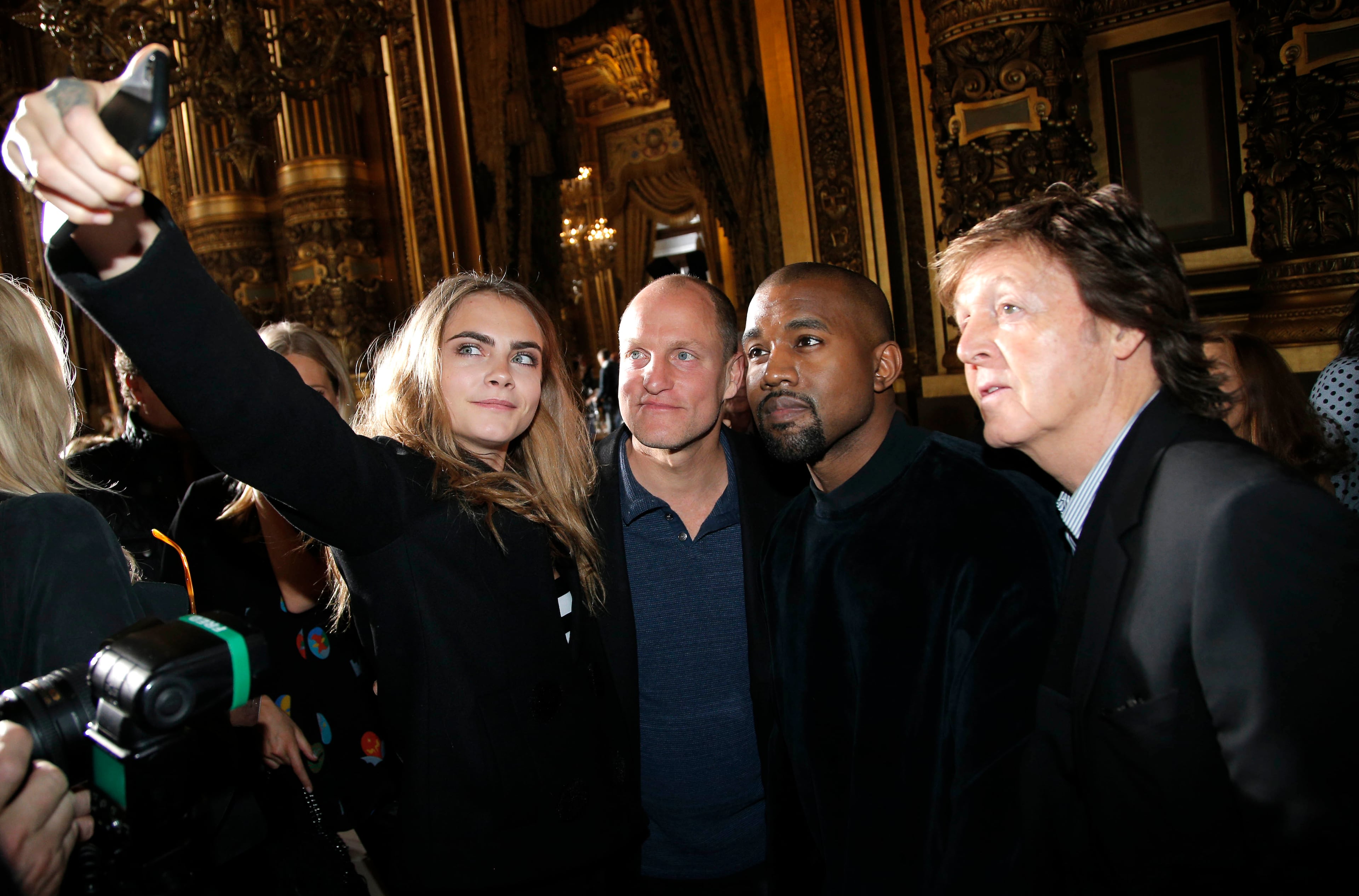 From left, model Cara Delevingne, takes a photographer with actor Woody Harrelson, singers Kanye West and Paul McCartney prior to Stella McCartney's ready to wear fall-winter 2015-2016 fashion collection during Paris Fashion Week, Paris, France, Monday, March 9, 2015. (AP Photo/Thibault Camus)