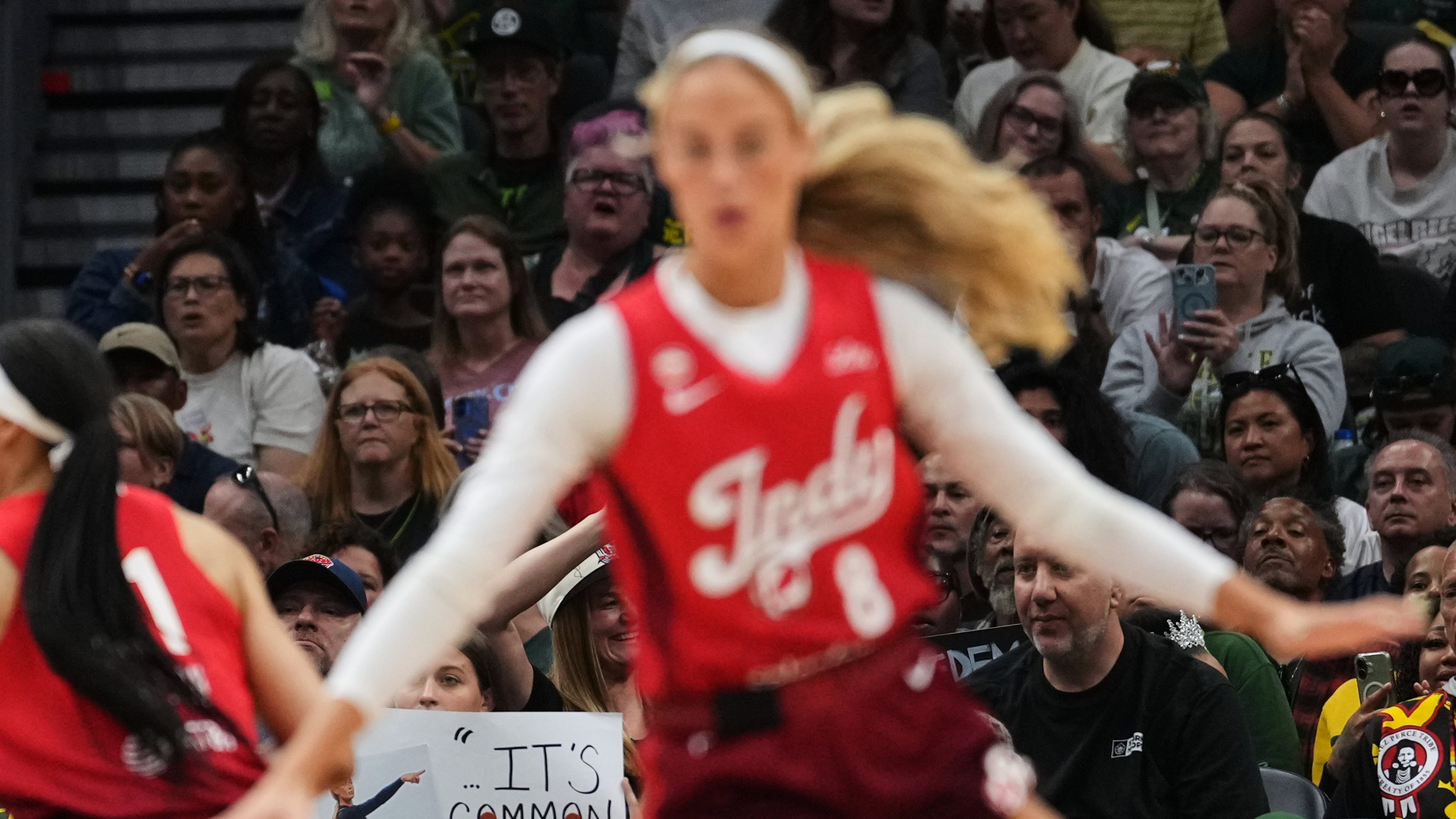 Indiana Fever guard Sophie Cunningham, front, runs by a fan holding a sign referencing her comments on transgender athletes and women's sports during the first half of a WNBA basketball game against the Seattle Storm, Tuesday, July 28, 2026, in Seattle. (AP Photo/Lindsey Wasson)