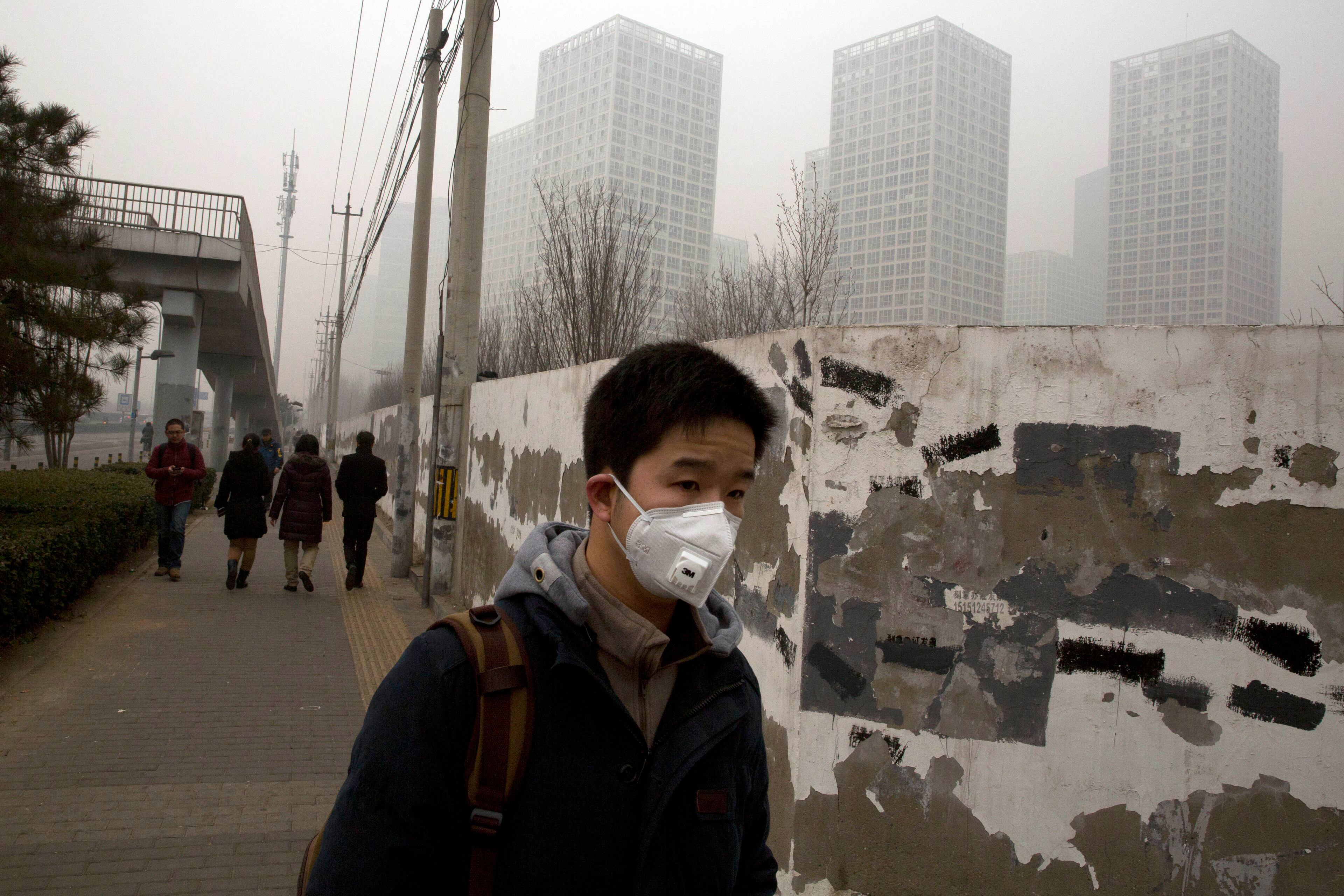 A man wears a mask during a hazy day in Beijing, China, Wednesday, Feb. 26, 2014. Beijing remained cloaked in hazardous white pollution hiding much of its skyline Wednesday, despite the announced closures or production cuts at 147 of the city's industrial plants.