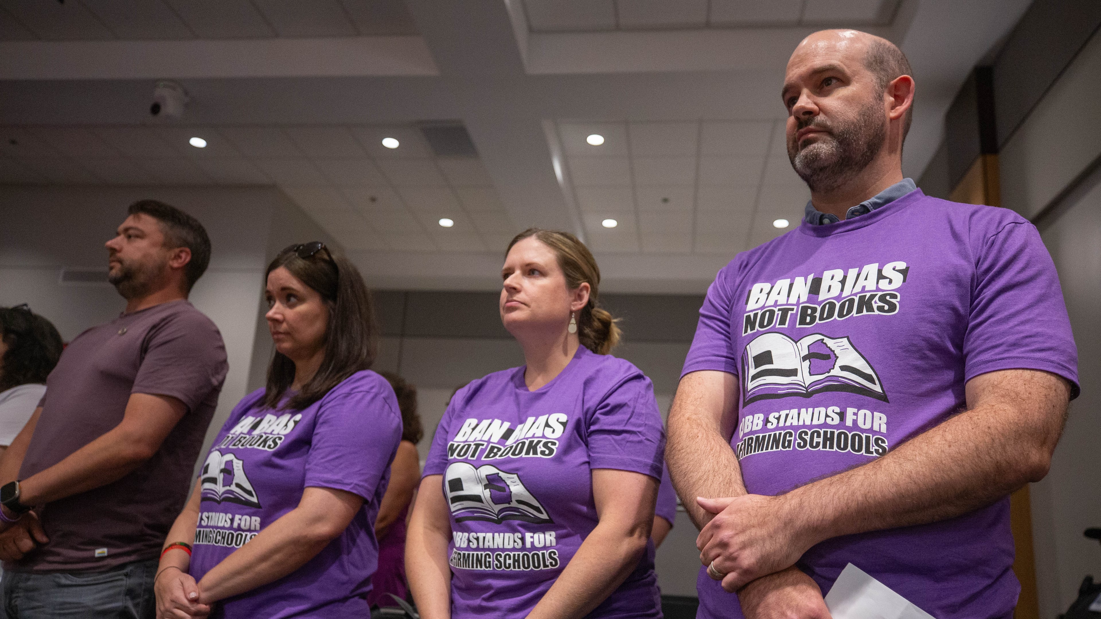At a Cobb school board meeting in July, demonstrators wore shirts calling for the district to "ban bias, not books" after a teacher was removed from her classroom for reading a book that challenges gender norms to fifth graders. At the board's most recent meeting in April, Superintendent Chris Ragsdale announced that four more books are being removed from school libraries for containing inappropriate content. (Katelyn Myrick / AJC file photo)