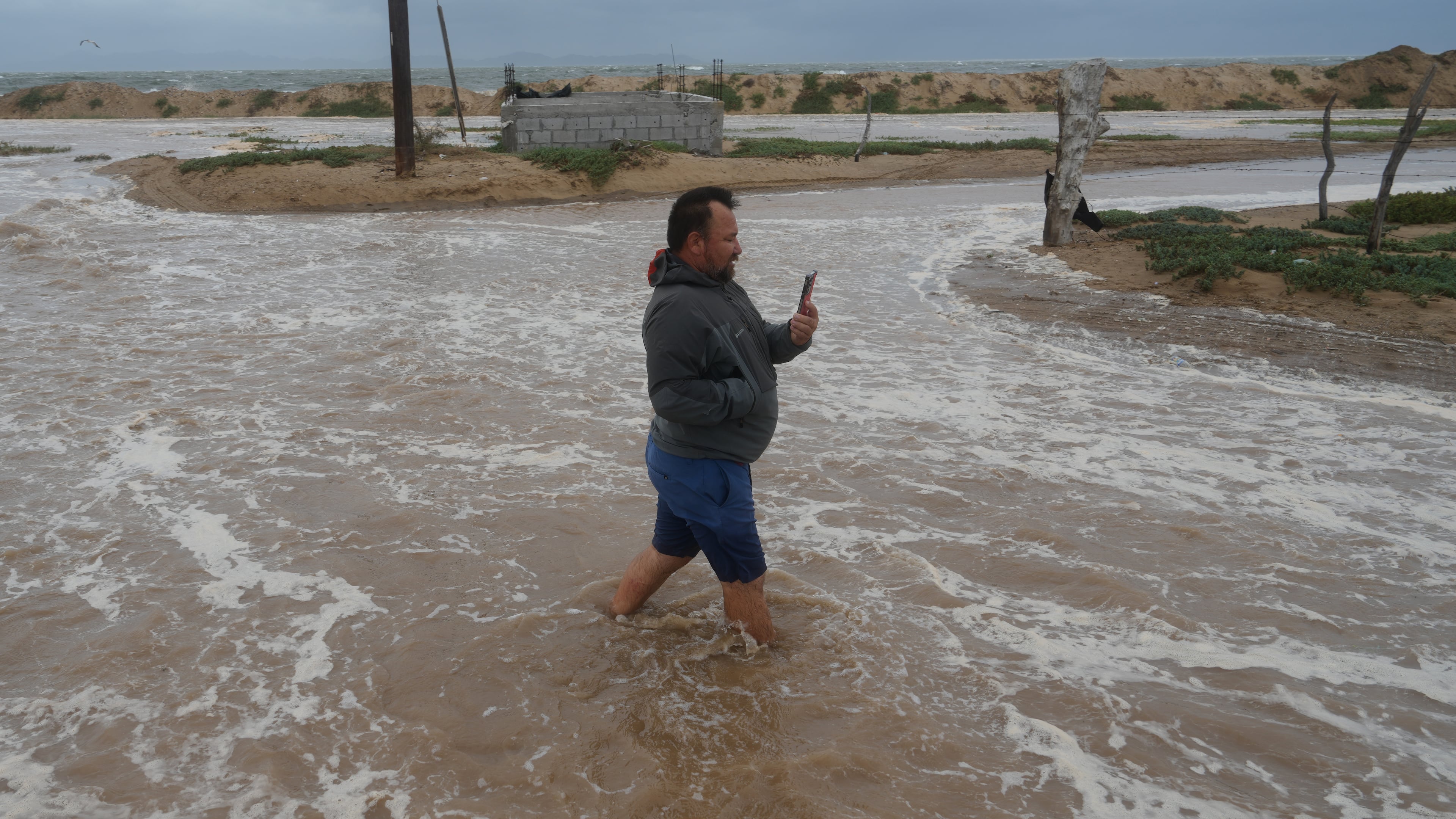 A man walks on a street next to the beach as he wades through water brought by Hurricane Polo in Puerto San Carlos, Baja California Sur state, Mexico, Monday, Sept. 28, 2026. (AP Photo/Eduardo Verdugo)