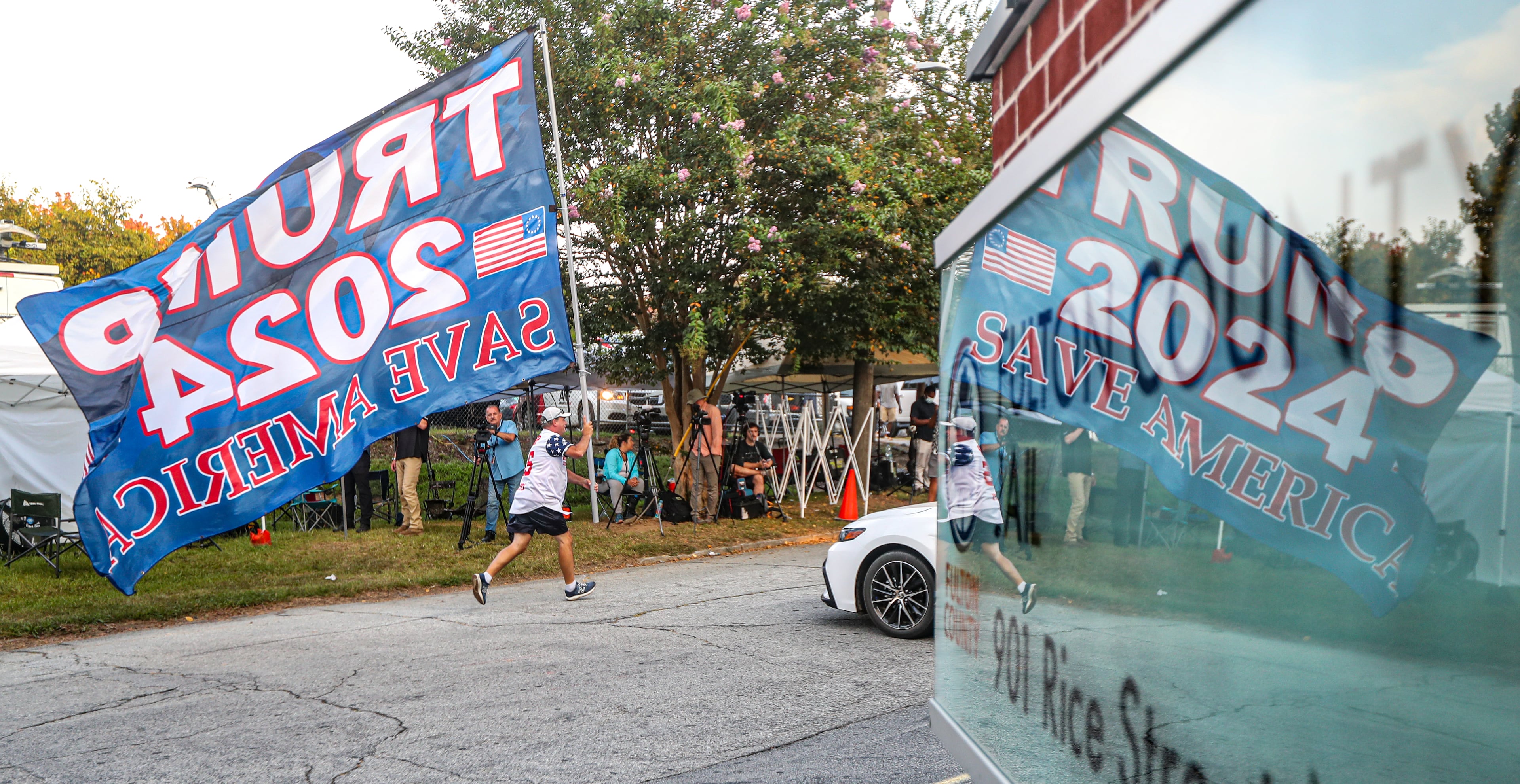 August 24, 2023 Atlanta: Mike Boatman from Evansville, Indiana carries a large Trump flag along Rice Street late Thursday morning, Aug. 24, 2023 where there were more than 100 protestors gathered outside the jail, and they were prepared to wait for hours until the anticipated arrival of former President Donald Trump this afternoon. (John Spink / John.Spink@ajc.com)