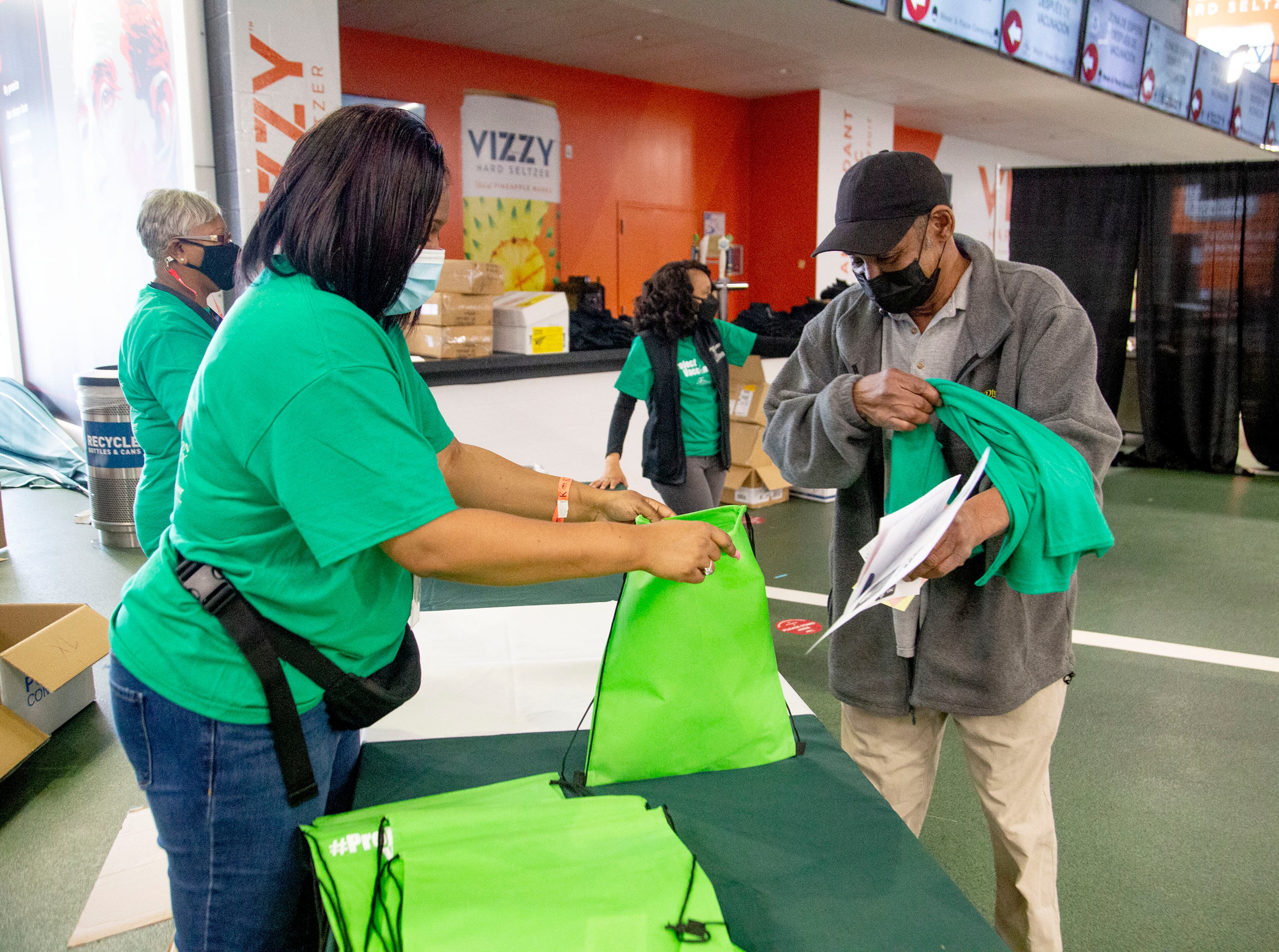 Fulton County Schools employee Lashanda Brown (left) hands out gift bags to people after receiving their vaccination shot at the Mercedes-Benz Stadium on Monday. STEVE SCHAEFER FOR THE ATLANTA JOURNAL-CONSTITUTION
