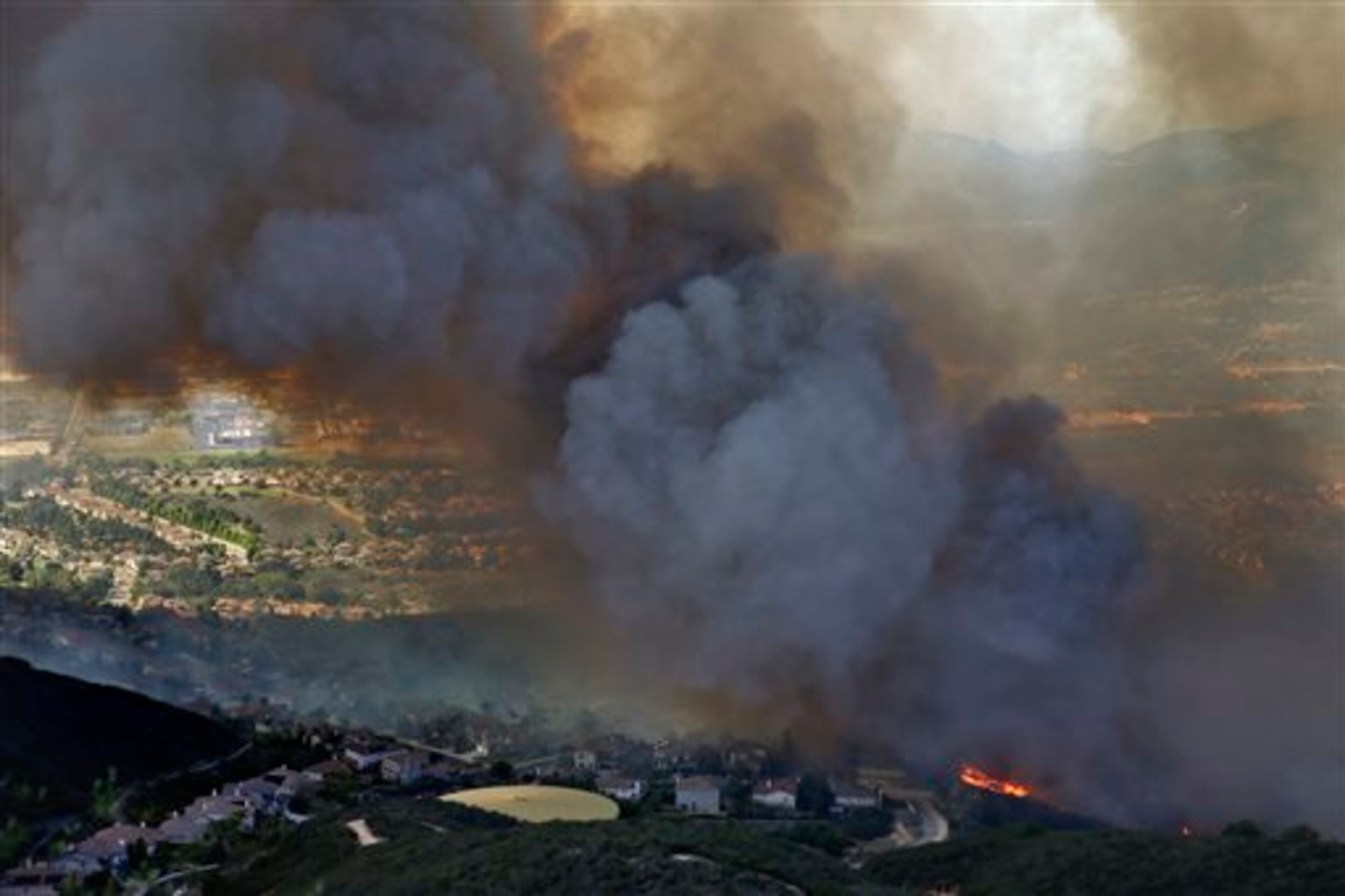 A wildfire approaches homes on Wednesday, May 14, 2014, in San Marcos, Calif. Flames engulfed suburban homes and shot up along canyon ridges in one of the worst of several blazes that broke out Wednesday in Southern California during a second day of a sweltering heat wave, taxing fire crews who fear the scattered fires mark only the beginning of a long wildfire season. (AP Photo)