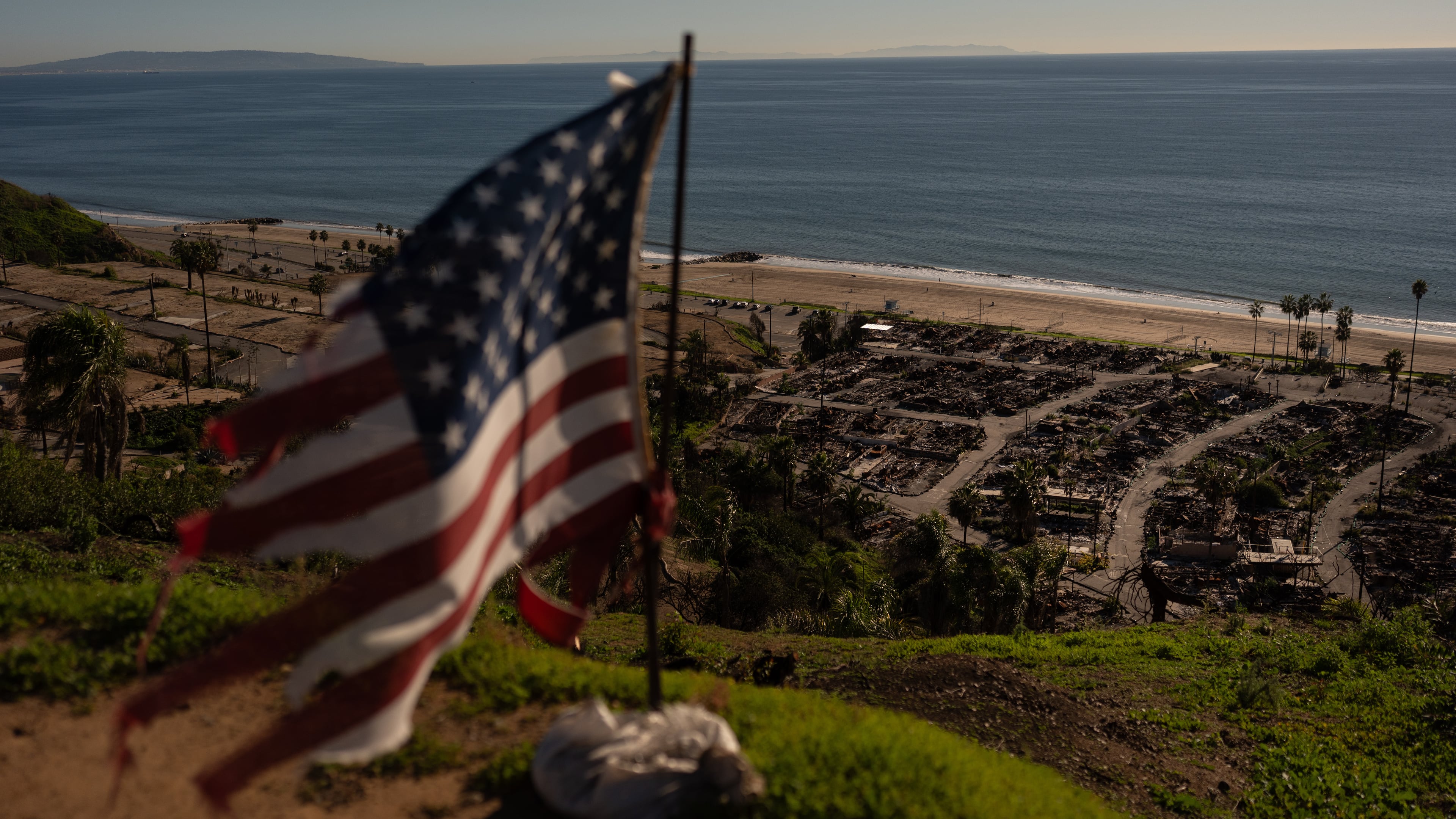 FILE - A tattered U.S. flag flaps in the wind over the remains of a mobile home park that was destroyed in the Palisades Fire along the Pacific Ocean, Dec. 5, 2025, in the Pacific Palisades neighborhood of Los Angeles. (AP Photo/Jae C. Hong, file)