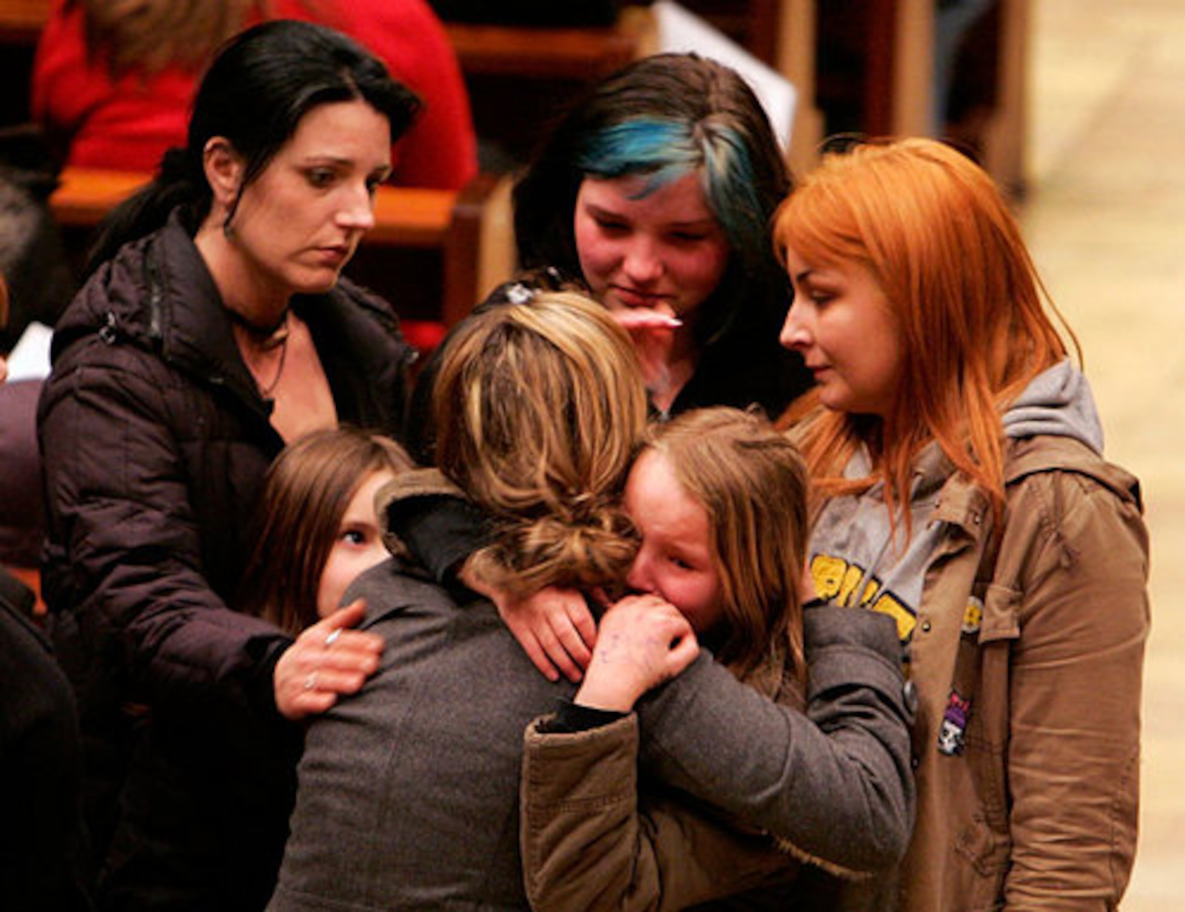 Mourners embrace each other in tears in a church during a memorial service.