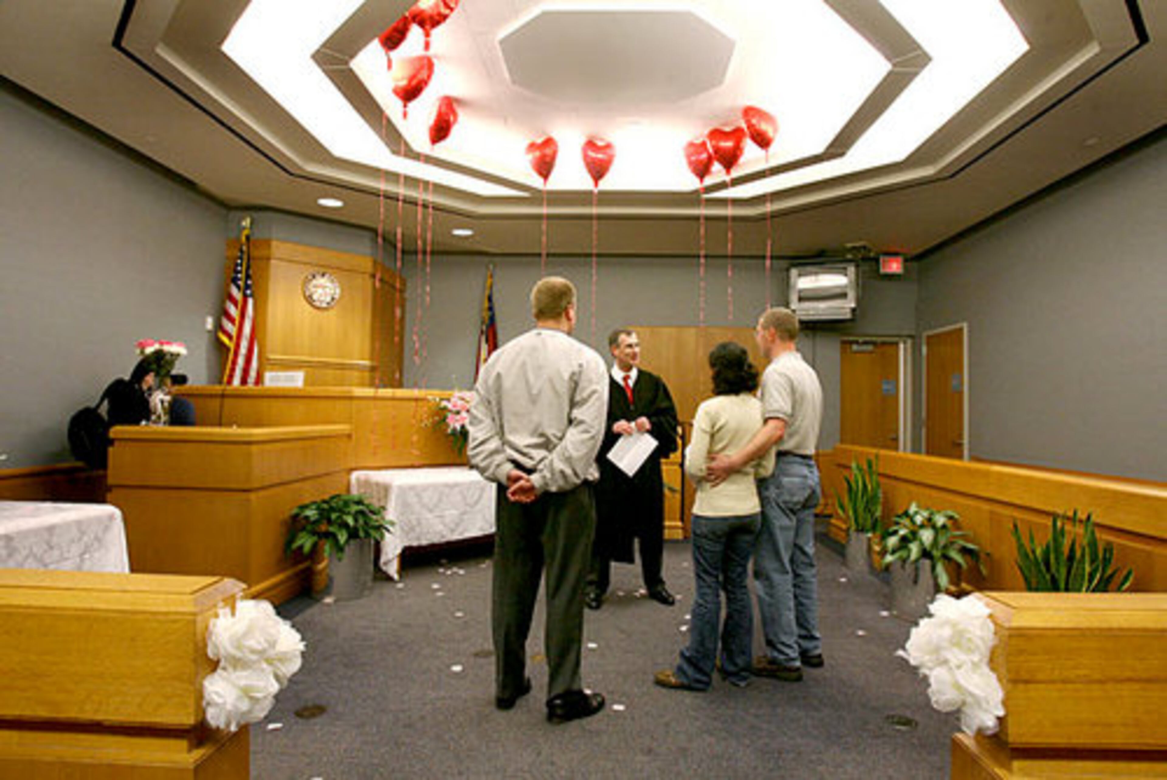 On a carpet sprinkled with rose petals, Gwinnett County Chief Magistrate George Hutchinson, III (center) officiates at the wedding ceremony of Carmen Urrutia and Scott Theumer as a friend of the couple looks on.