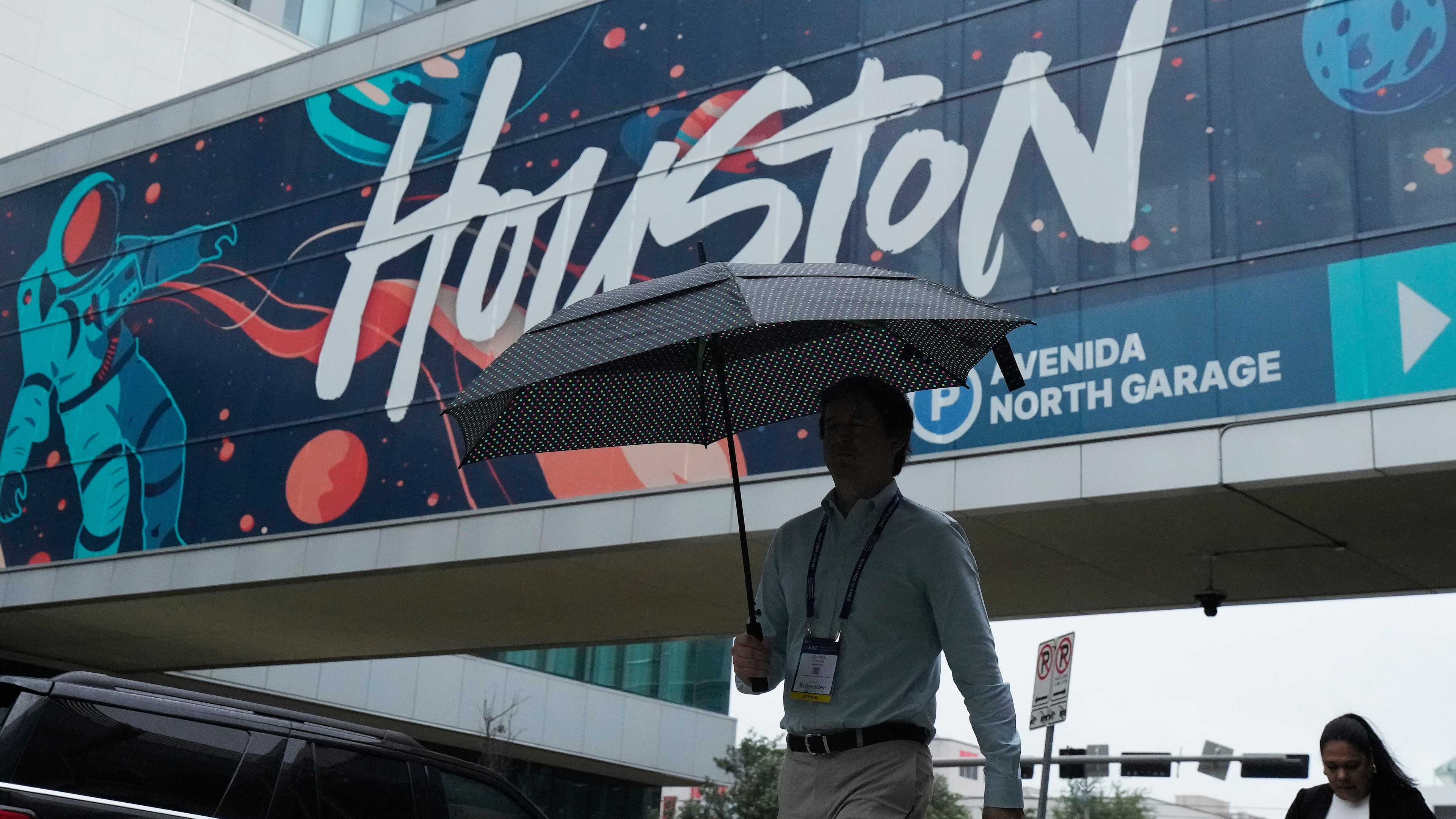 A convention attendee walk through the rain outside the George R. Brown Convention Center, Wednesday, June 17, 2026, in Houston. (AP Photo/Kevin M. Cox)