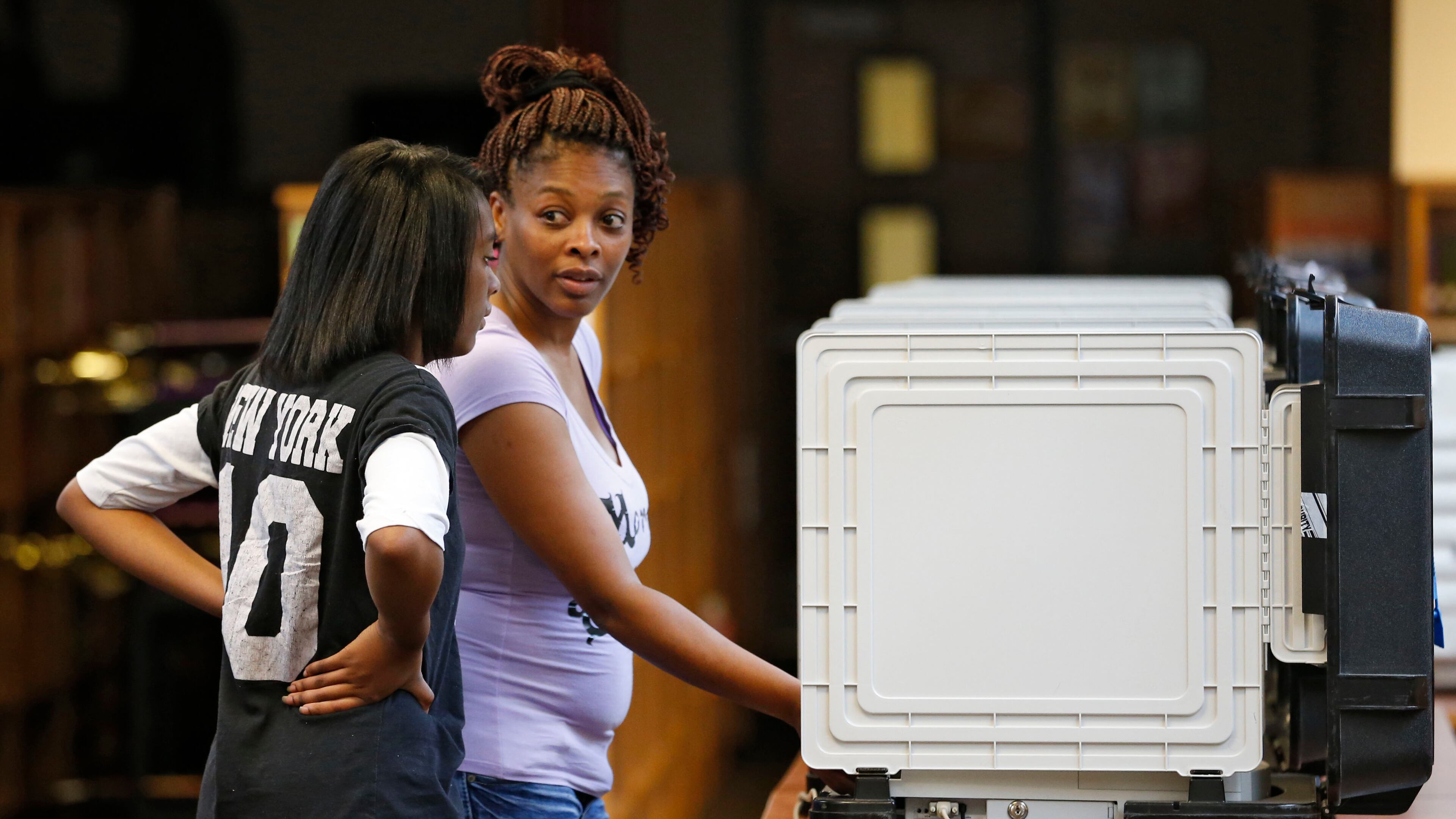 Zhane Johnson, 14, watches as her mother, Cassandra, casts her ballot at Mary Mcleod Bethune Middle School in Decatur in July. BOB ANDRES / BANDRES@AJC.COM