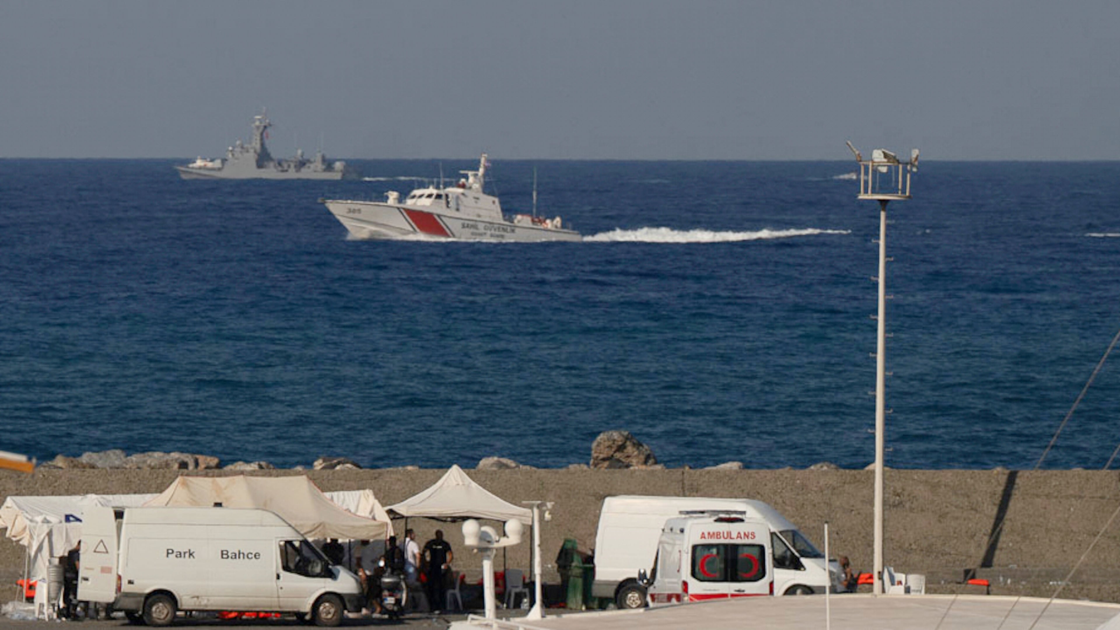 Vessels sail near the port of Kyrenia as an ambulance is parked on the waterfront in the Turkish-occupied northern part of Cyprus, Sunday, Aug. 30, 2026, after a catamaran-style ferry overturned off the island's northern coast. (AP Photo/Nedim Enginsoy)