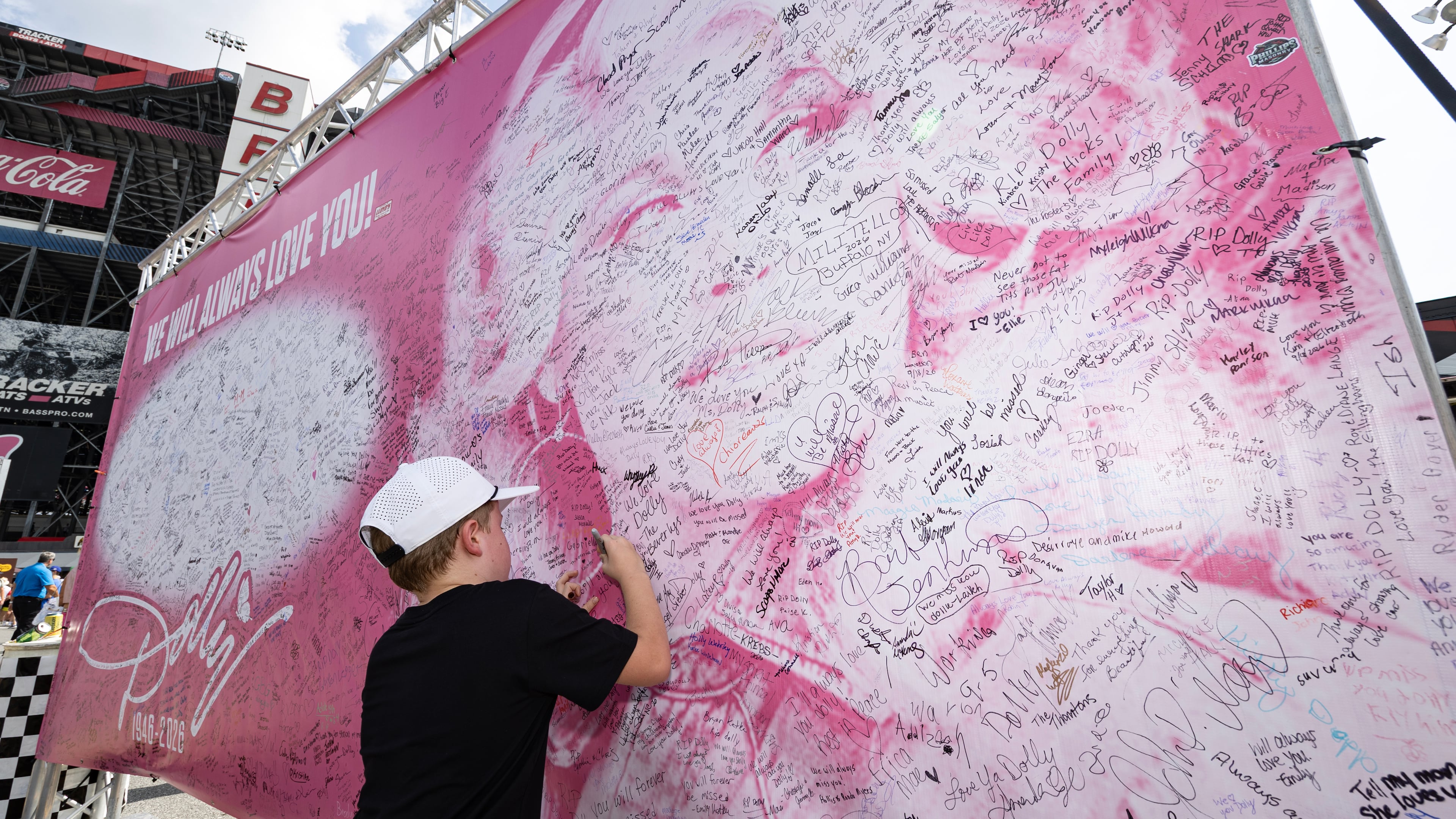 Henry Bailey, 7, from Kentucky signs his name to a tribute sign to the late Dolly Parton before a NASCAR Cup Series auto race Saturday, Sept. 19, 2026, in Bristol, Tenn. (AP Photo/Wade Payne)