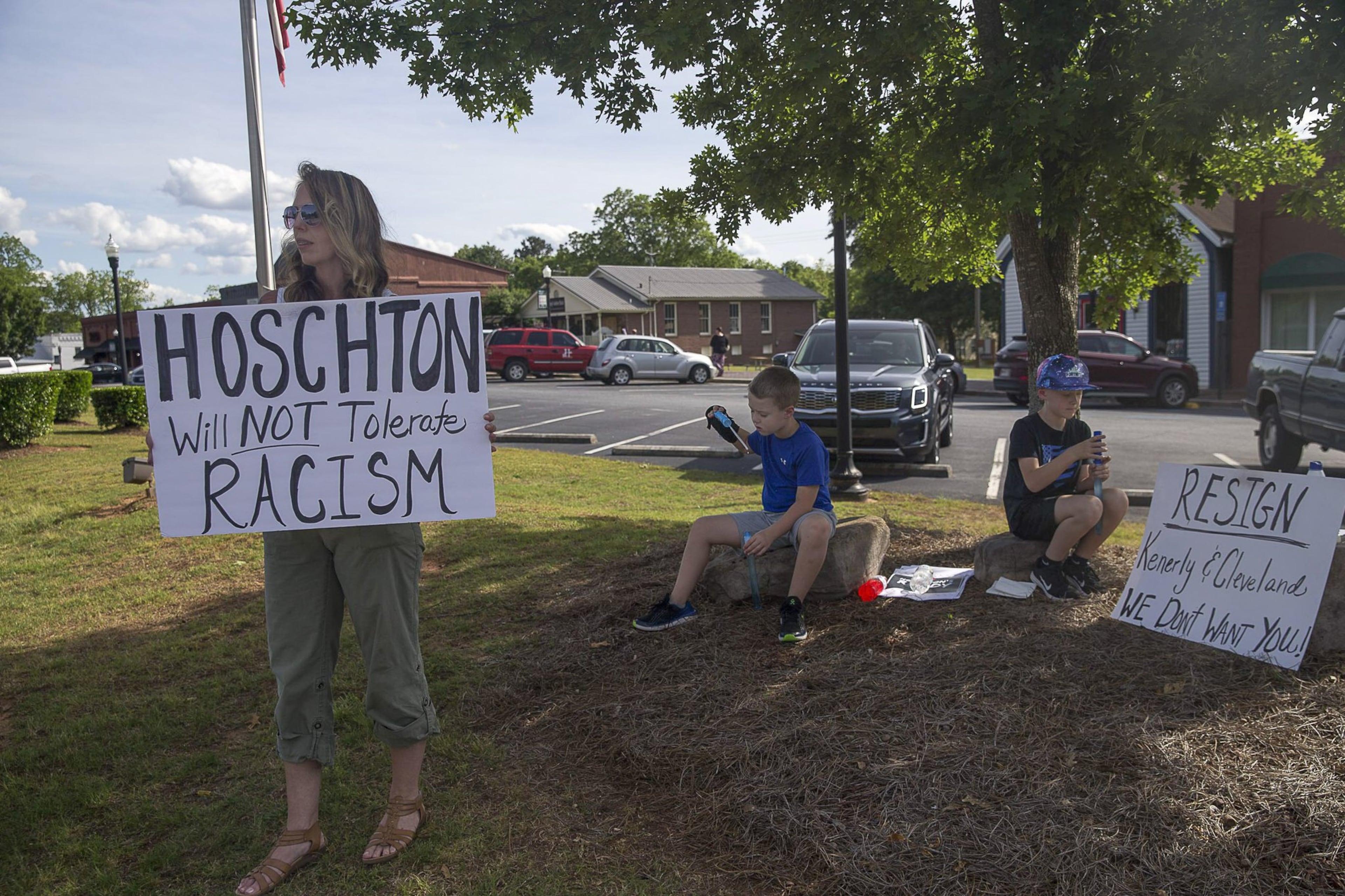 Hoschton resident Kelly Winebarger protests for the resignation of Hoschton Mayor Theresa Kenerly and Councilman Jim Cleveland as her sons Ryder (center) and Knox (right) sit quietly by the roadside in Hoschton, Monday, May 6, 2019. “I don’t want people the think that about our community,” Kelly said as she referenced the controversy concerning the mayor of Hoschton allegedly pulling the resume of Keith Henry from a packet of four finalists for a city position, “because he is black, and the city isn’t ready for this.”(ALYSSA POINTER/ALYSSA.POINTER@AJC.COM)
