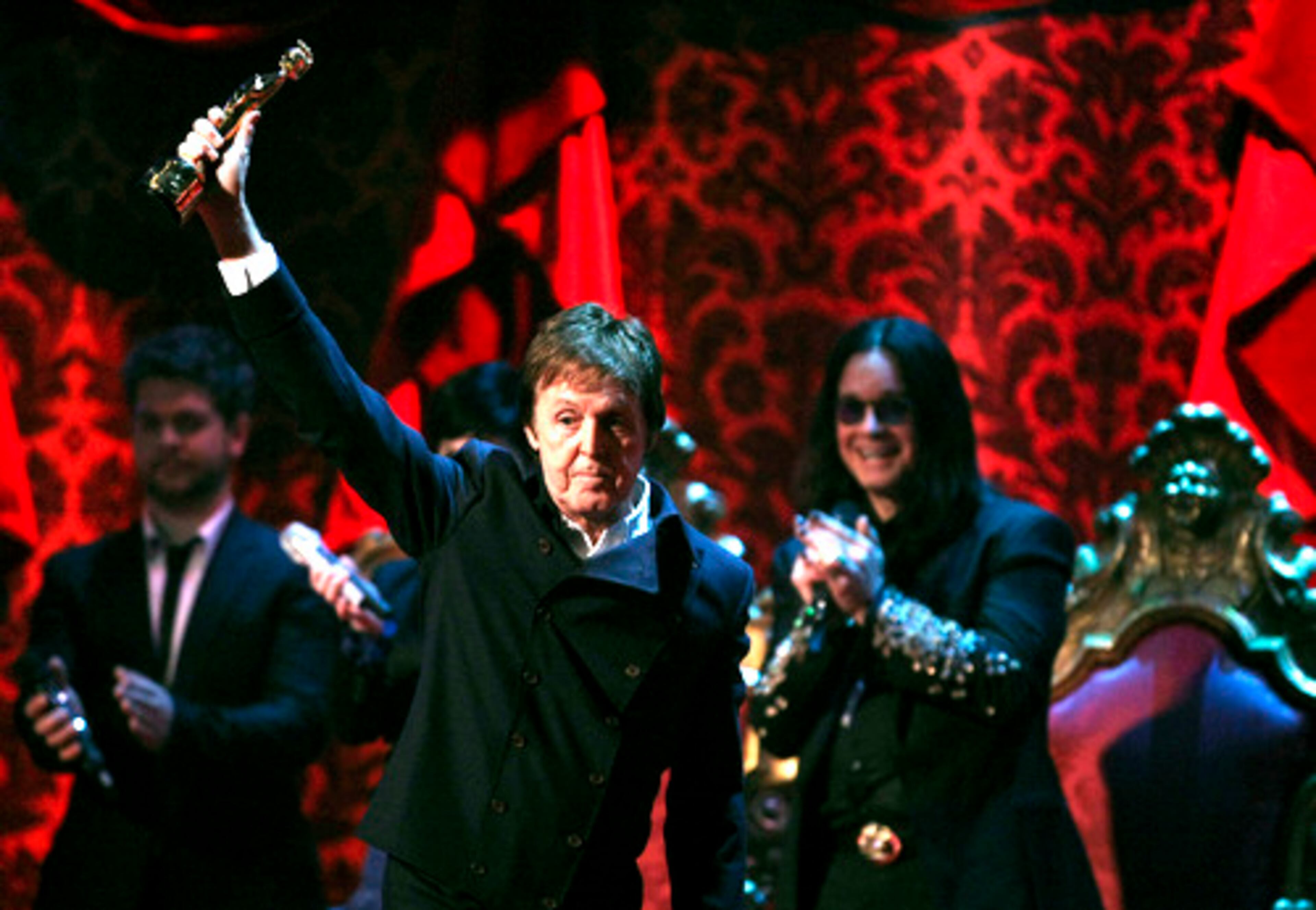 McCartney holds up his Outstanding Contribution to Music Award. Jack Osbourne (left background) and Ozzy Osbourne (right background) applaud him.
