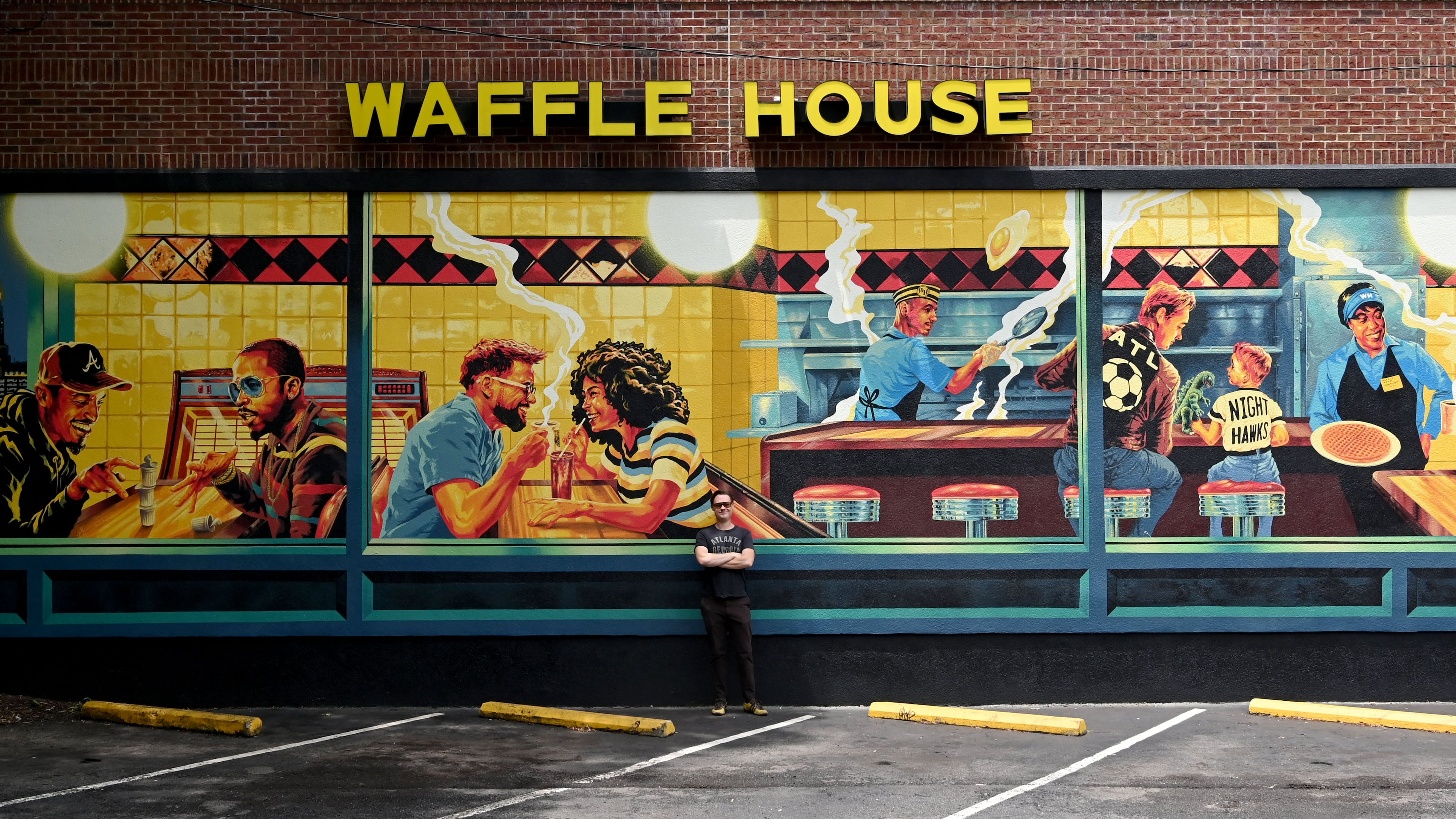 Artist Nick Benson poses for a portrait in front of his mural, commissioned by Downtown Atlanta Inc., near Centennial Park, on Thursday, May 21, 2026, in Atlanta. Benson created the work as an Atlanta homage to Edward Hopper’s iconic painting "Nighthawks." (Hyosub Shin/AJC)