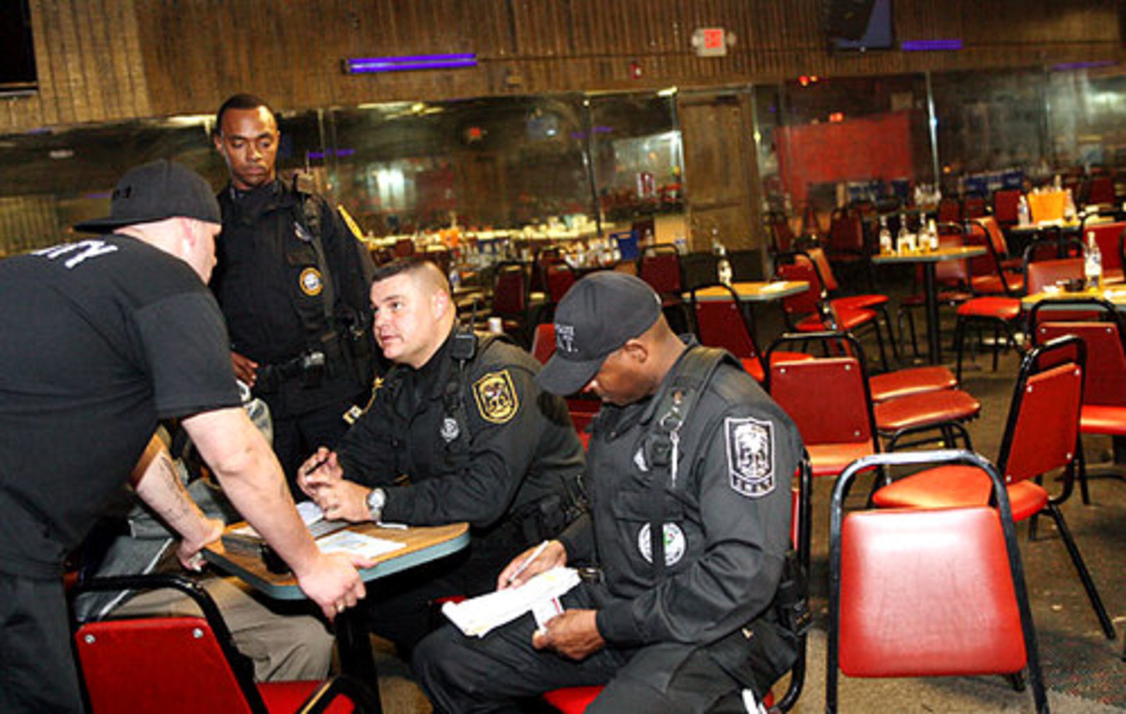 DeKalb County Police shut down El Noa Noa for not having a state liquor or business license on display. Steven Lehman (left), who works security for the club, learns that he needs to have a permit to work as a bouncer. Lt. R. Franklin (standing) listens as Detective R.E. Viar (second from right) issues Lehman a citation. Meanwhile, Detective J. Conley, (right) writes other citations to the club.