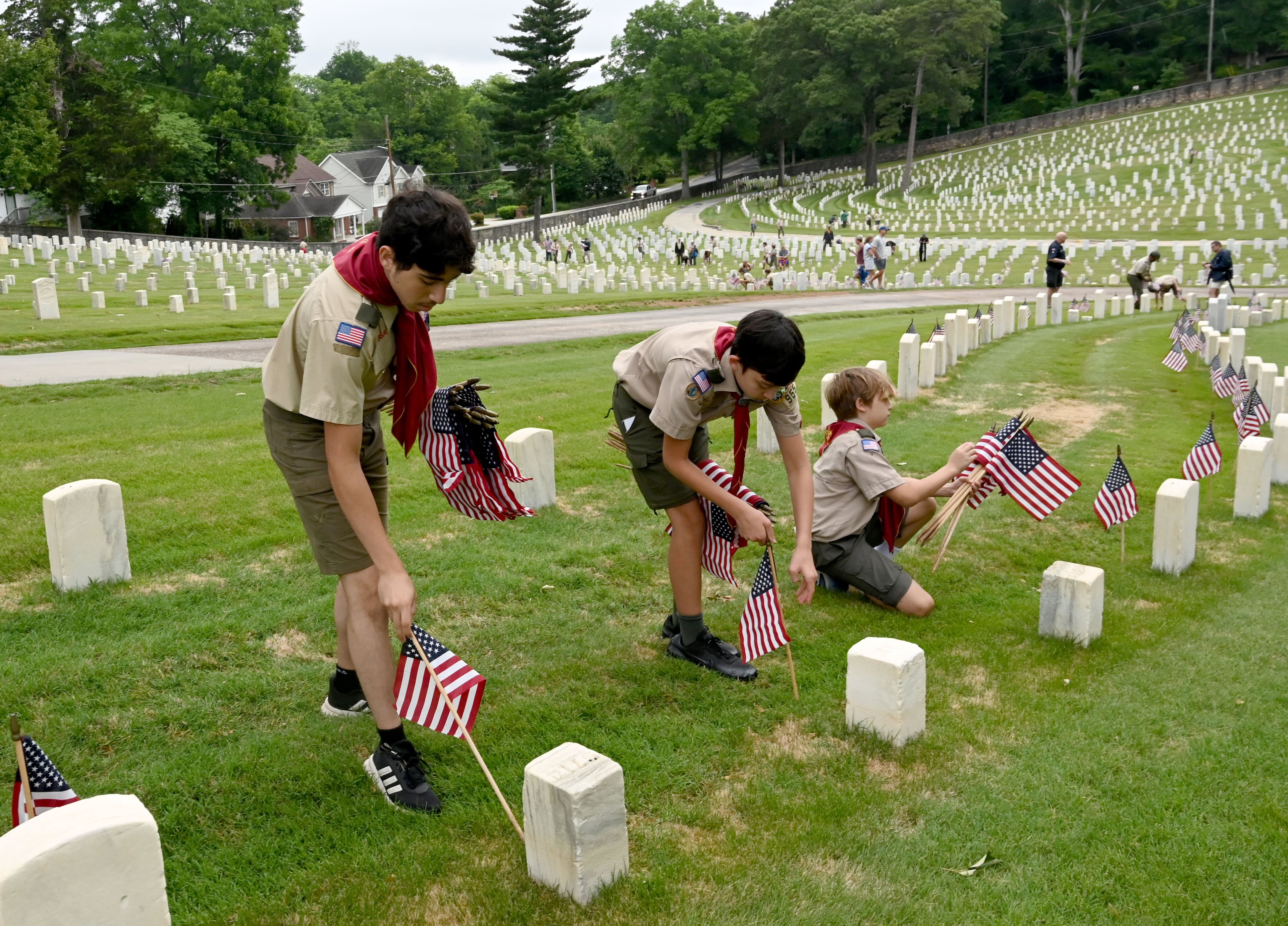 Scouts place a flag in front of a headstone during the Memorial Day Flag Placement event at Marietta National Cemetery on Saturday, May 23, 2026, in Marietta. Scouting groups in the community place more than 18,000 U.S. veteran grave flags at Marietta National Cemetery each year on the Saturday before Memorial Day, helping prepare for Monday’s ceremony. The long-running service project—organized with the National Memorial Day Association of Georgia—also gives youth and adults an opportunity to honor fallen service members and learn about their sacrifices and the area’s history. (Hyosub Shin/AJC)