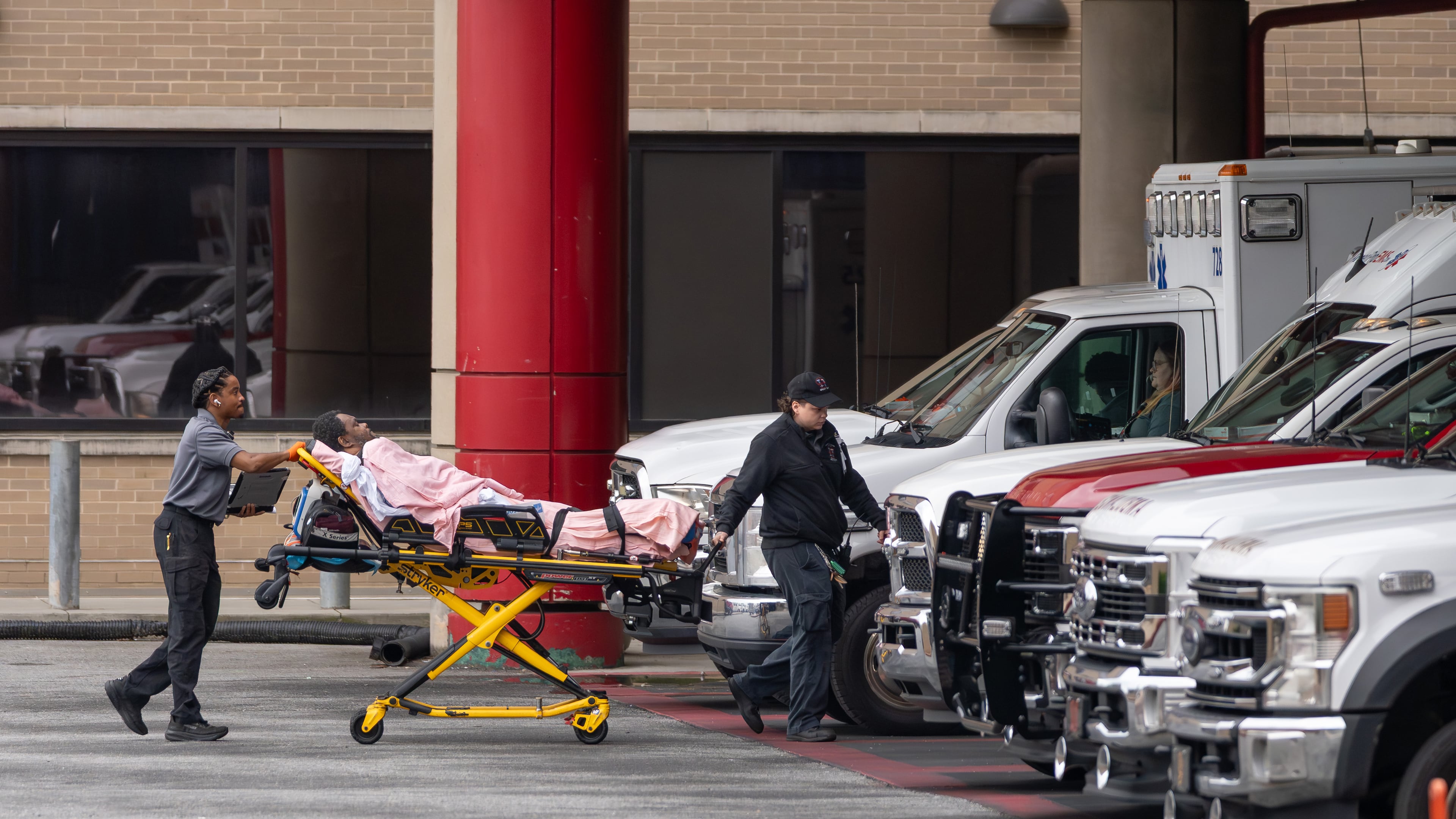 A medical crew wheels a patient across the parking area into Grady Memorial Hospital after parking across the street because the ambulance bay was full on Friday, May 1, 2026. (Ben Hendren for the AJC)