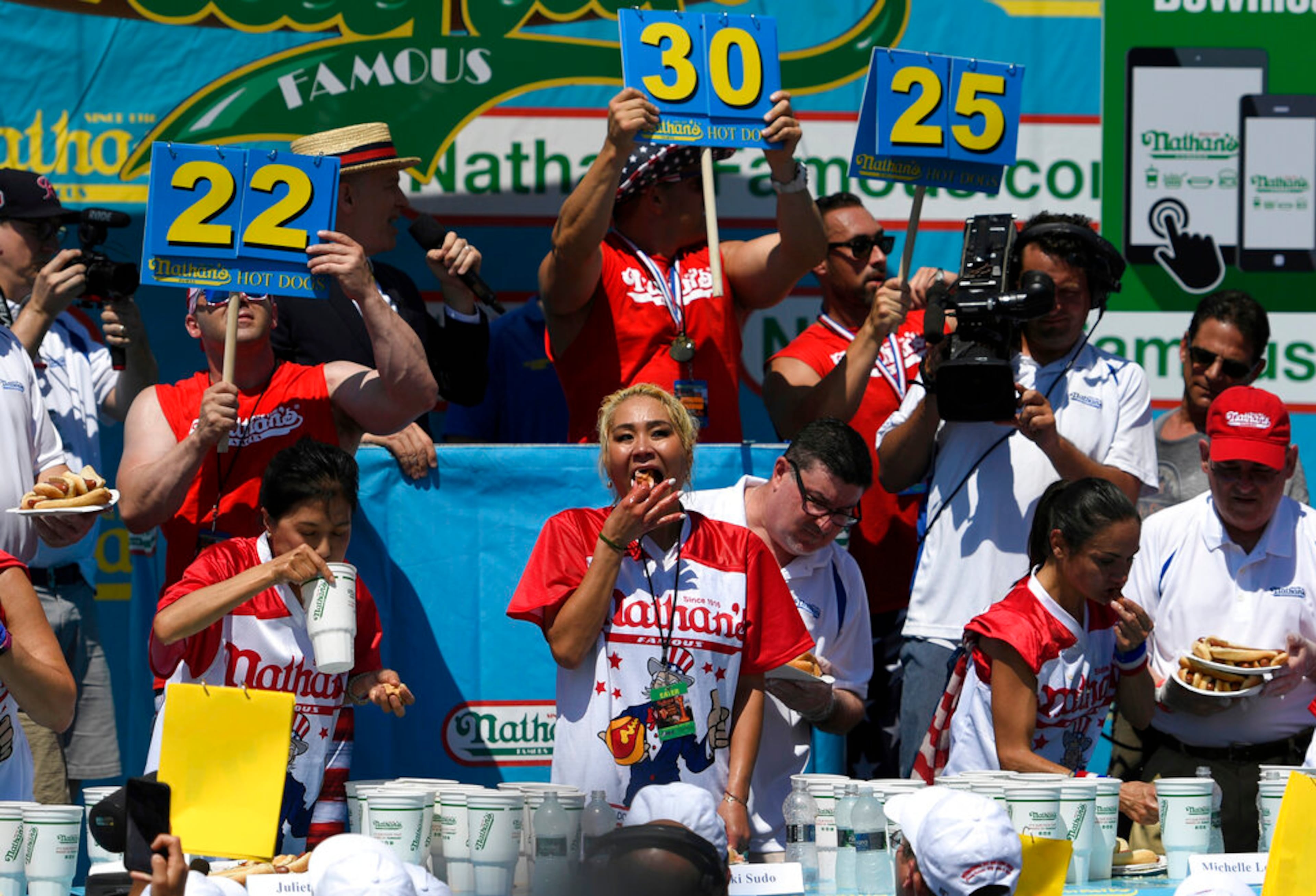 Juliet Lee, left, Miki Sudo, center, and Michelle Lesko, right, compete in the closing moments of the women's competition of the Nathan's Famous July Fourth hot dog eating contest, Thursday, July 4, 2019, in New York's Coney Island. (AP Photo/Sarah Stier)